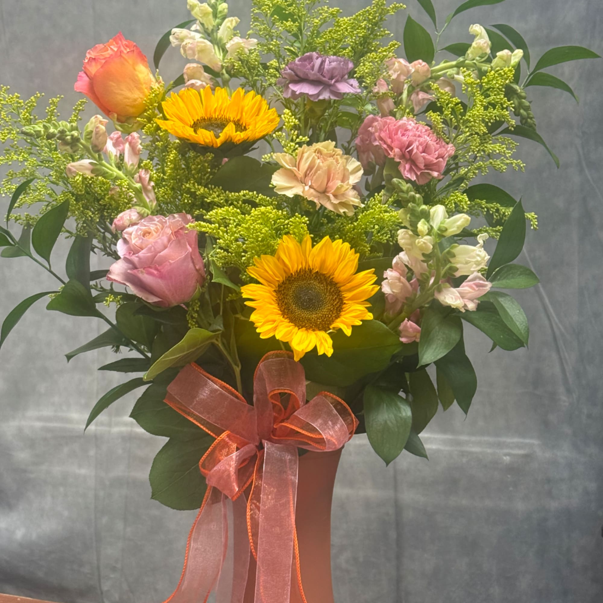 Mixed bouquet with sunflowers, roses, and pink carnations in a vase with ribbon