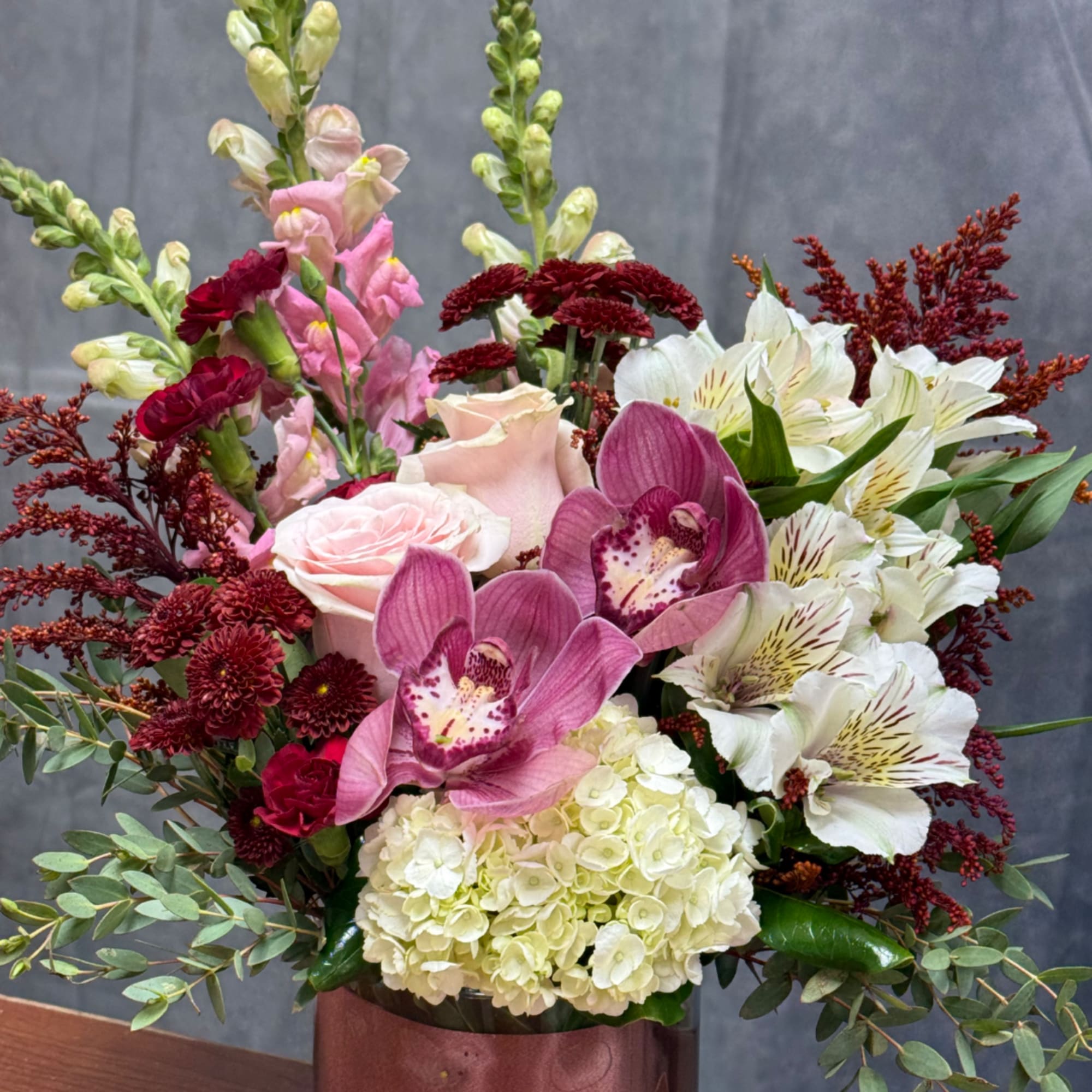 Mixed bouquet with pink orchids, white lilies, roses, and burgundy flowers in a vase