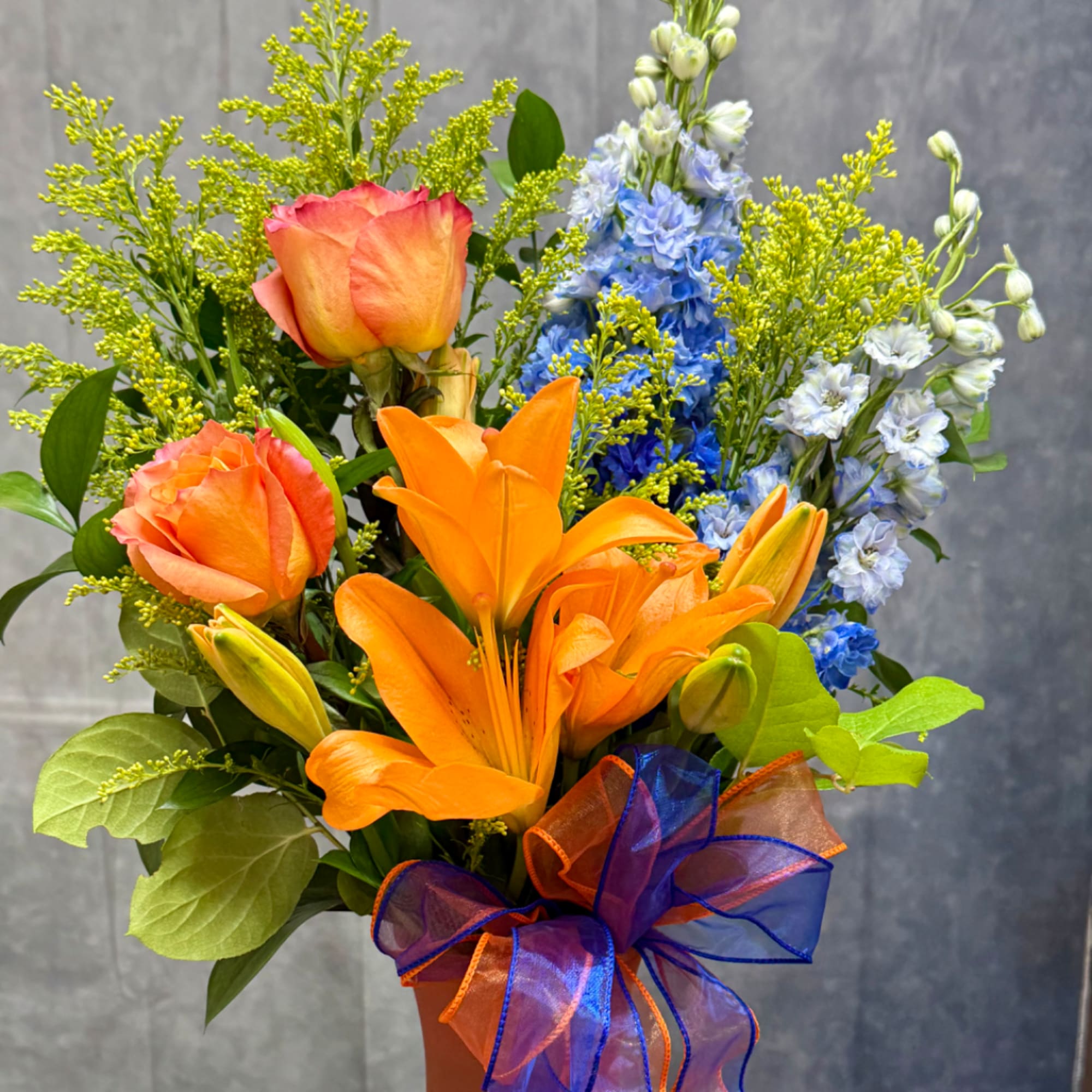 Orange roses and lilies with blue flowers in a wrapped bouquet