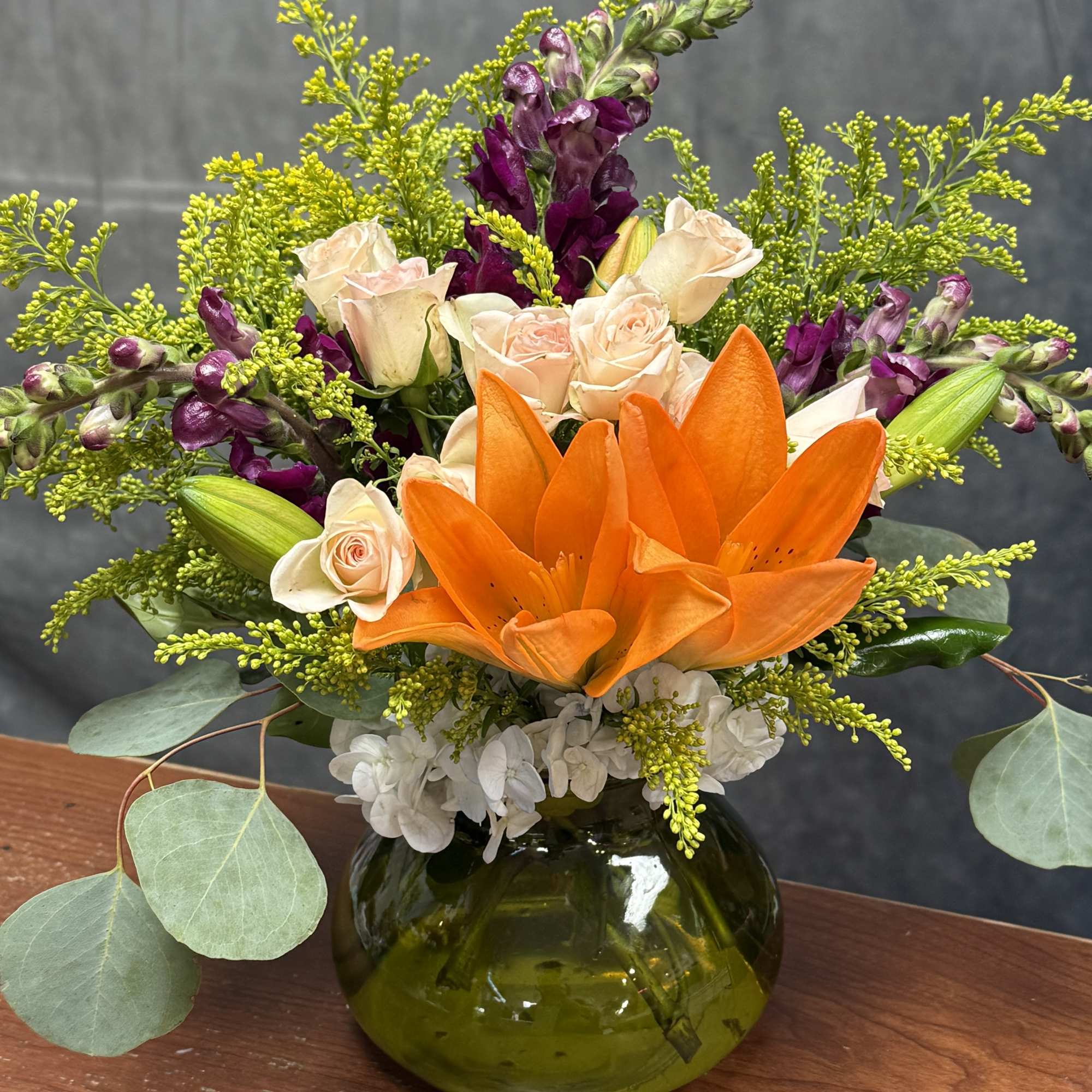 Orange lilies and pale roses in a green glass vase