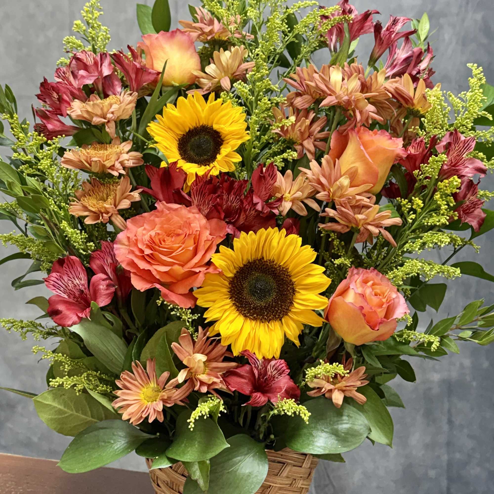 Basket arrangement with sunflowers, orange roses, and mixed blooms