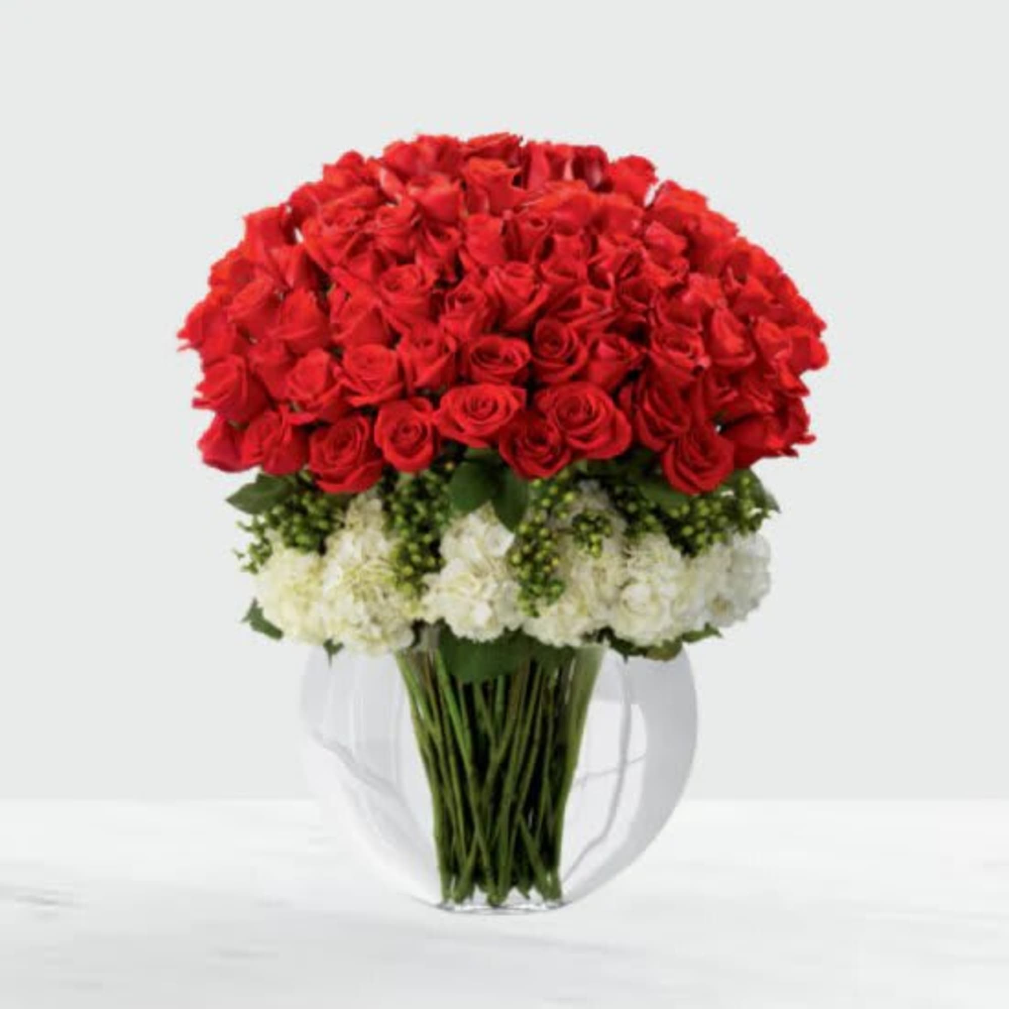 Red roses and white flowers arranged in a clear glass pitcher vase