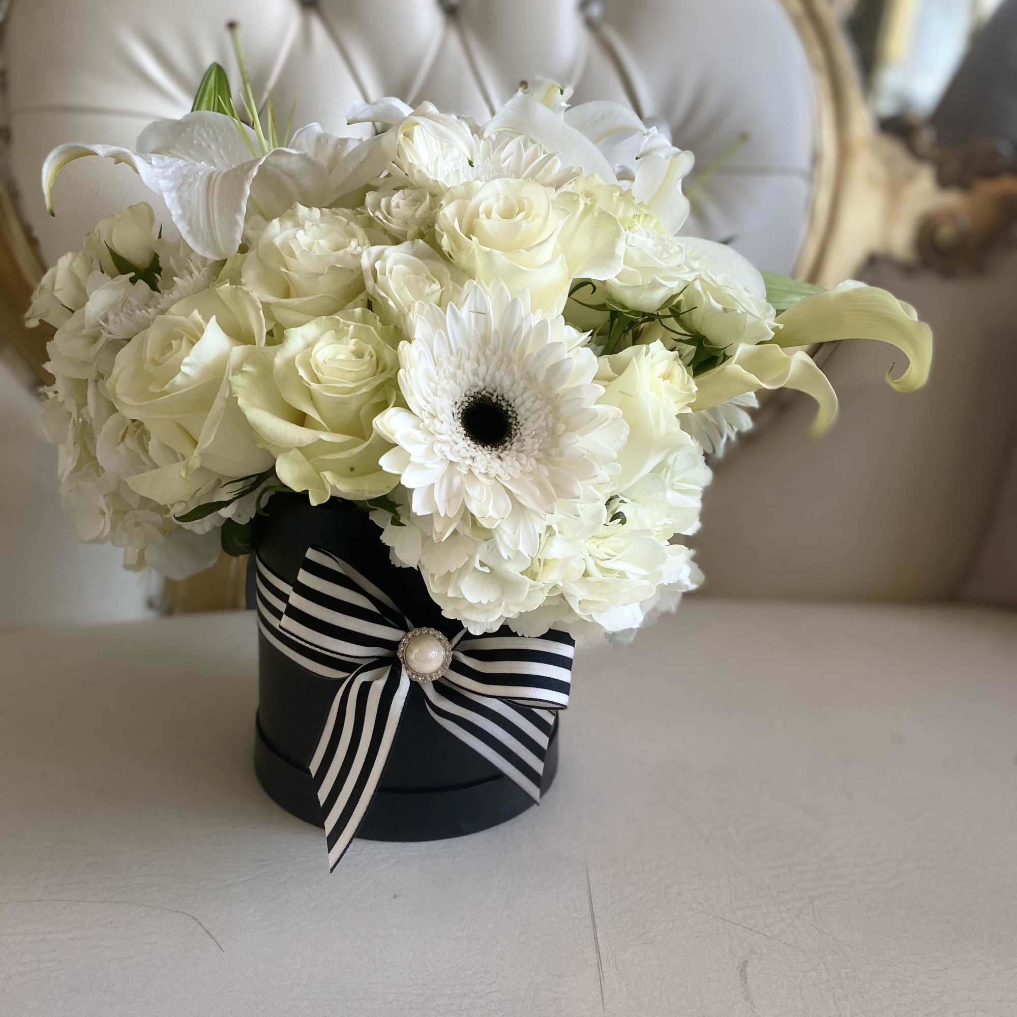 White rose and lily bouquet in a black hat box with striped ribbon