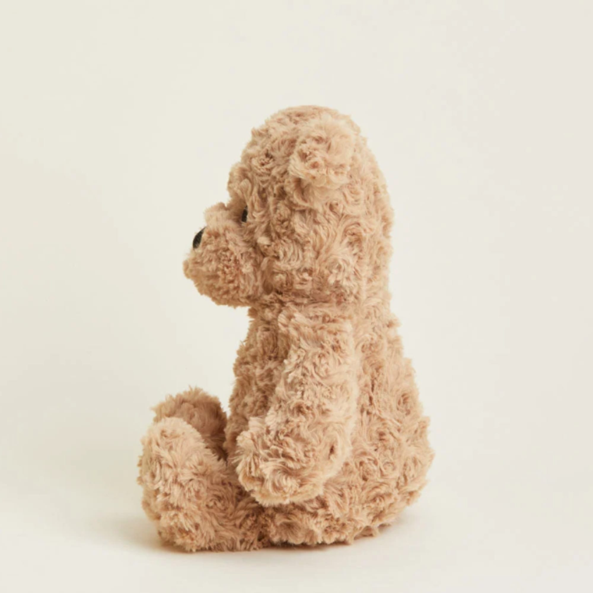Small tan plush teddy bear sitting in profile on a plain background