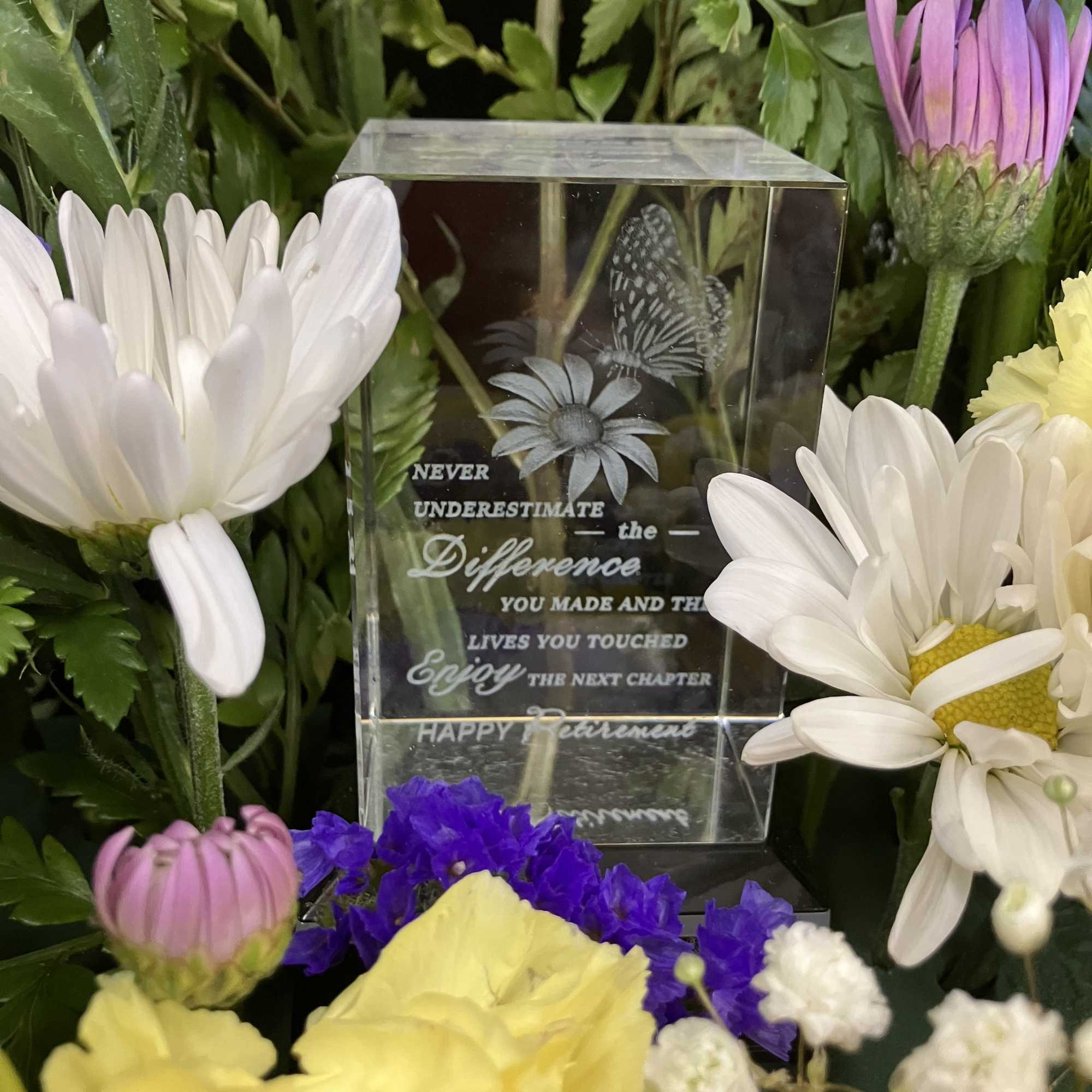 Mixed flowers surround a clear memorial keepsake block.
