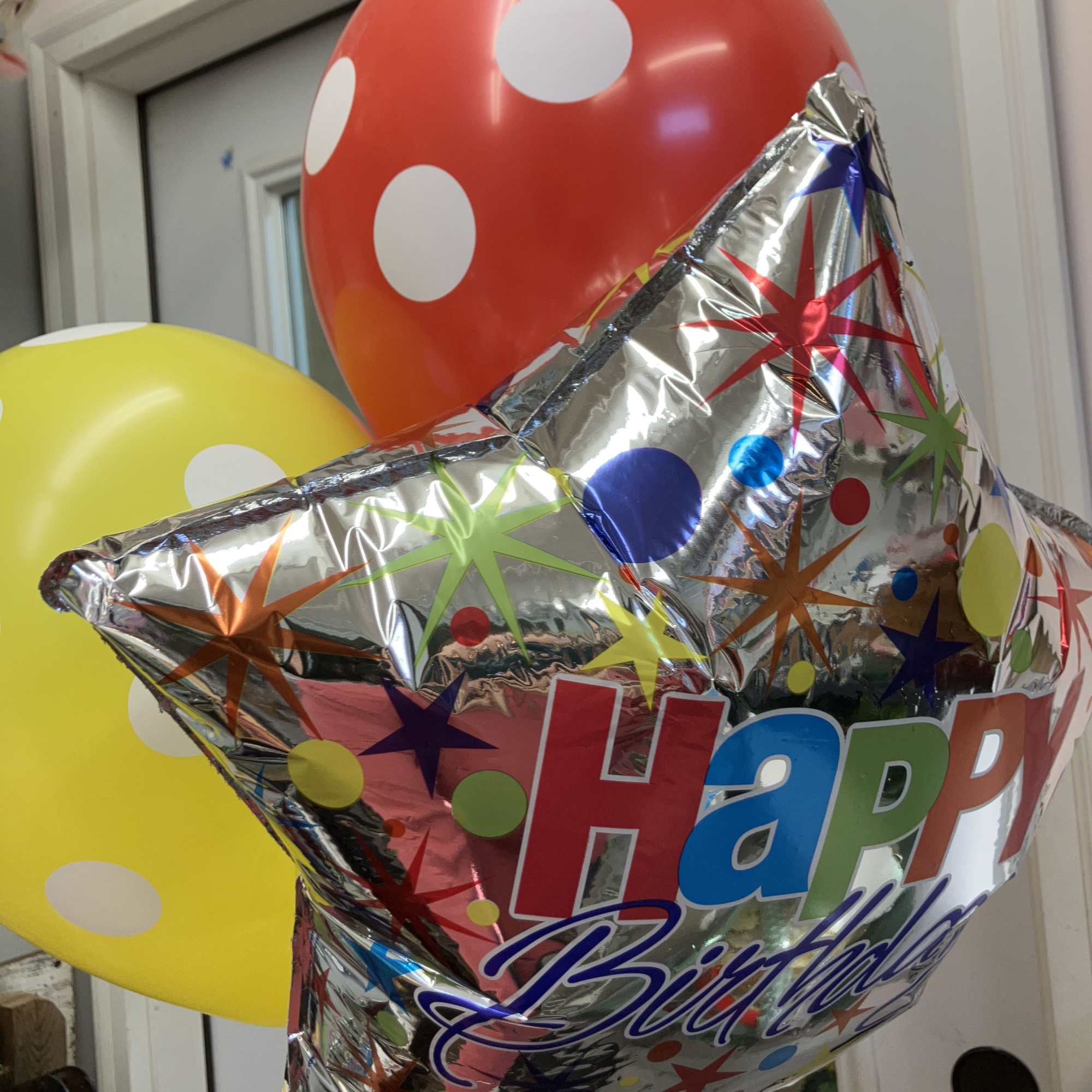 Birthday balloons including a silver star and red and yellow polka-dot balloons