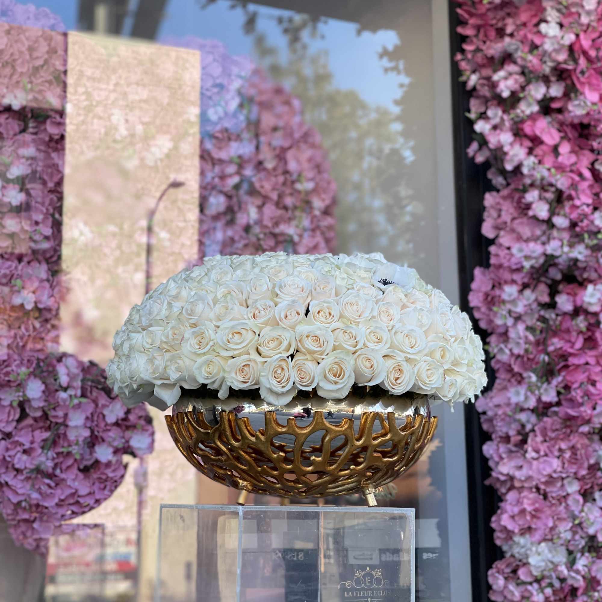 White rose arrangement in a gold decorative bowl on a clear pedestal