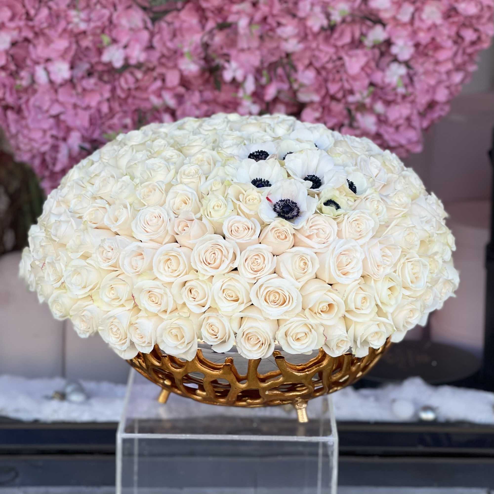 Round bouquet of white roses with a few white anemones in a gold vase