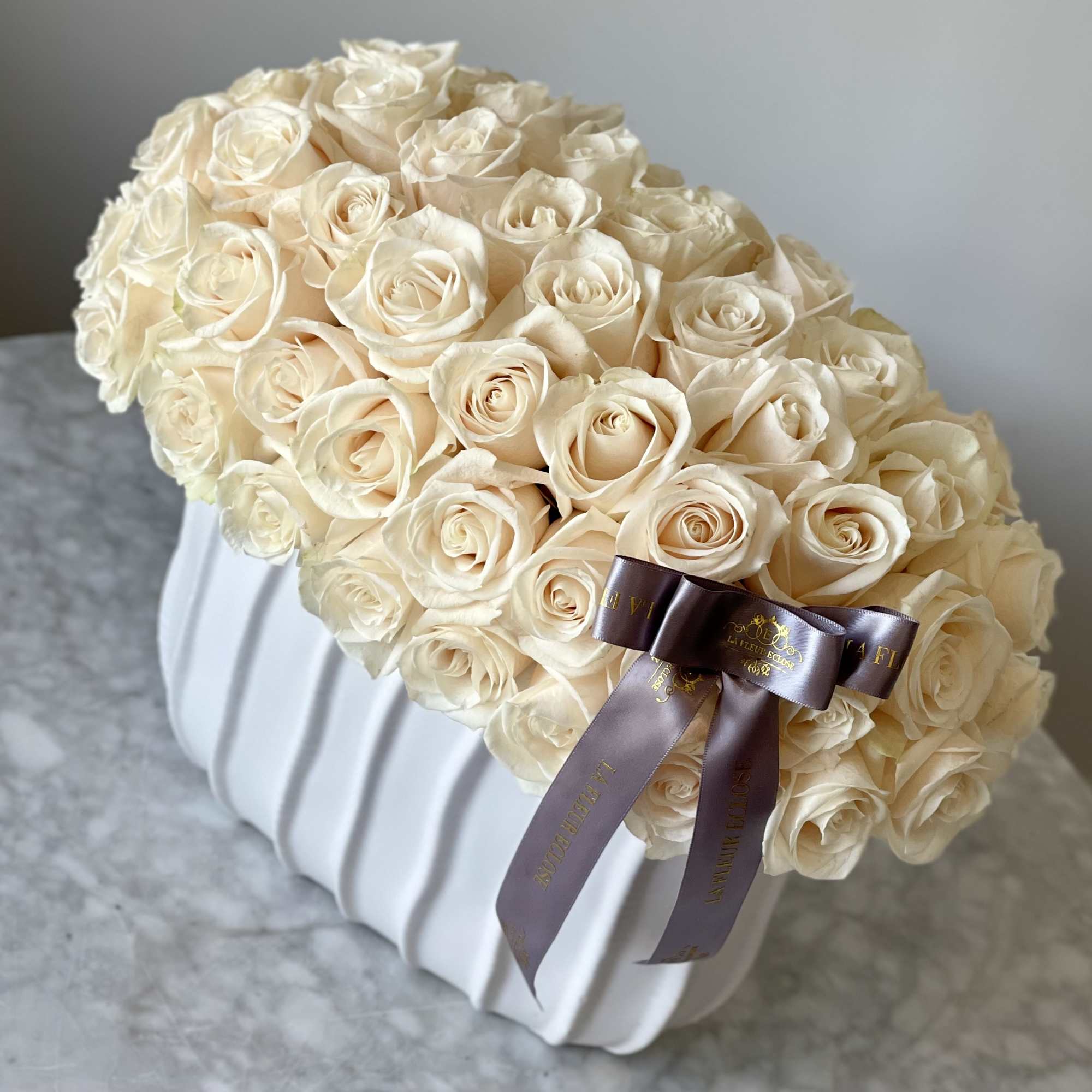 Cream rose bouquet in a white ribbed vase with a dark ribbon bow