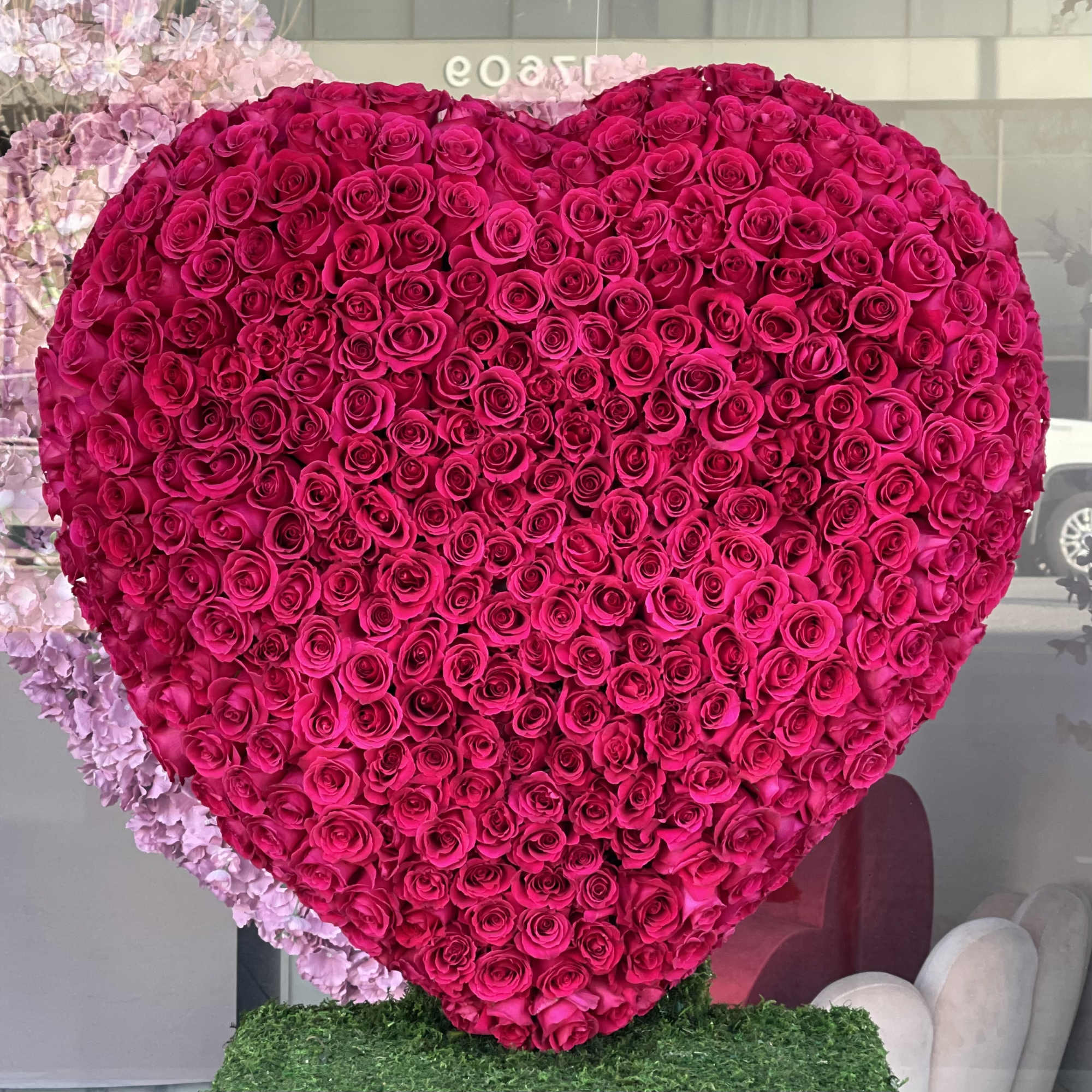 Heart-shaped arrangement of hot pink roses with pale pink flowers behind it