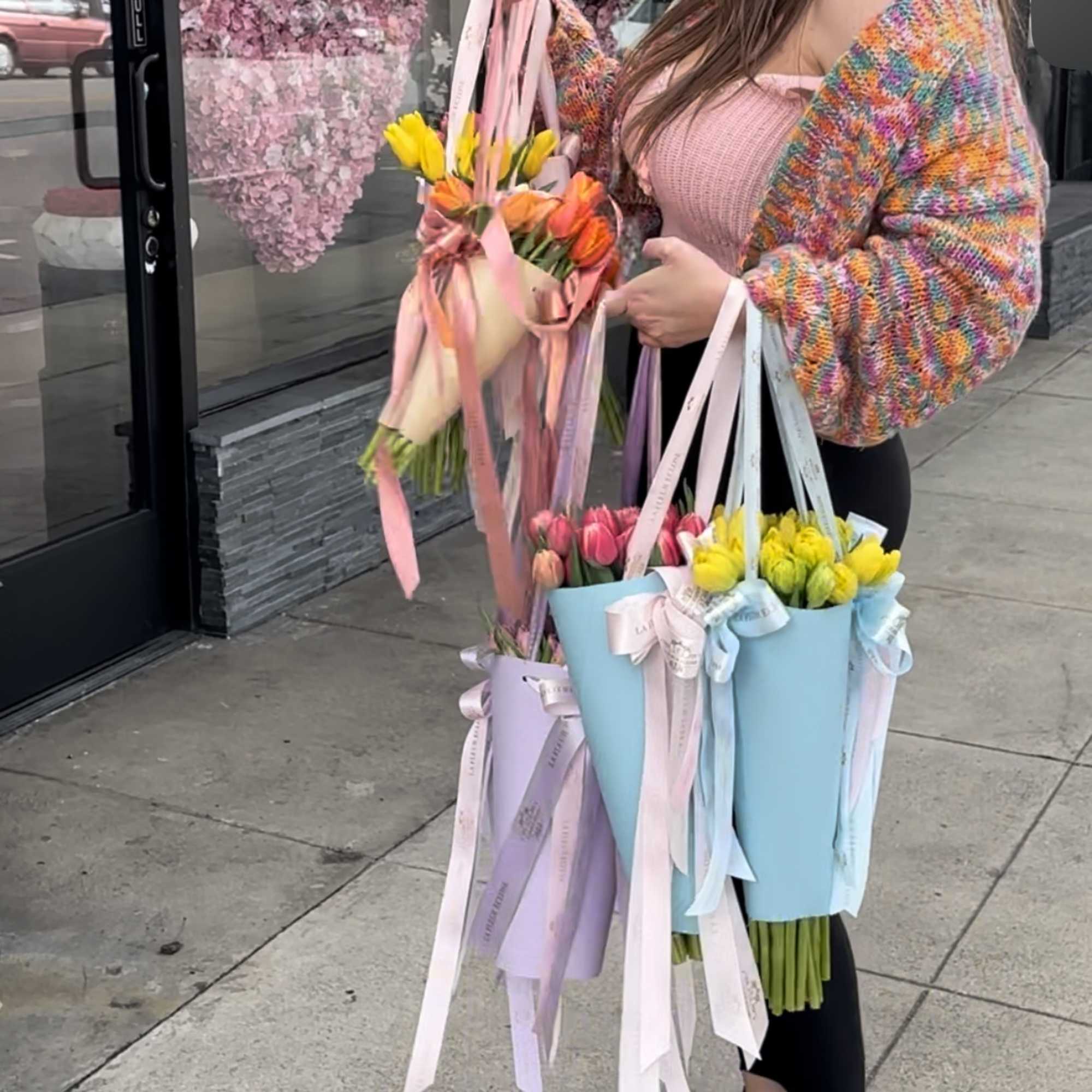 Person holding pastel tulip bouquets wrapped in ribboned paper bags