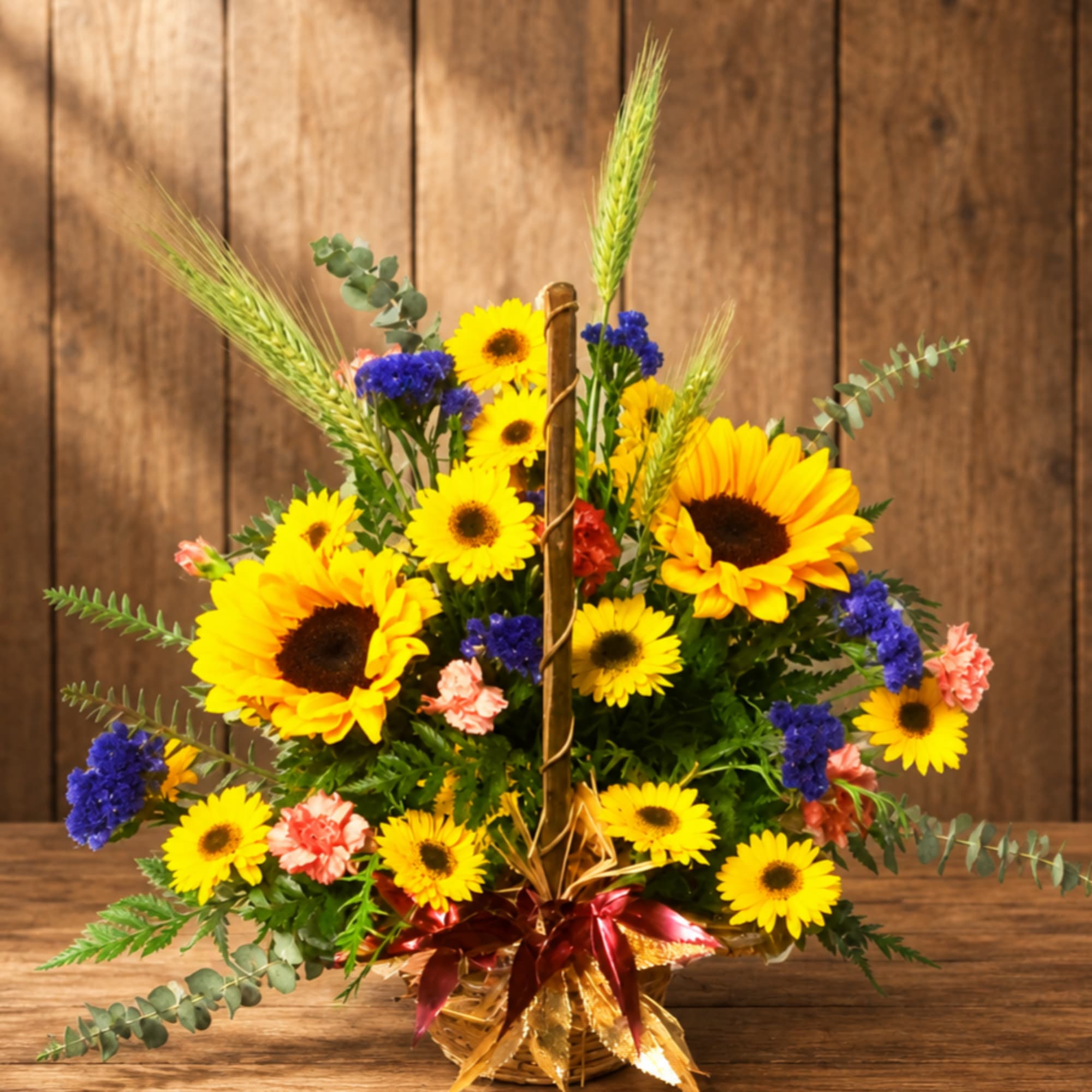 Basket arrangement of yellow sunflowers, blue flowers, and pink carnations