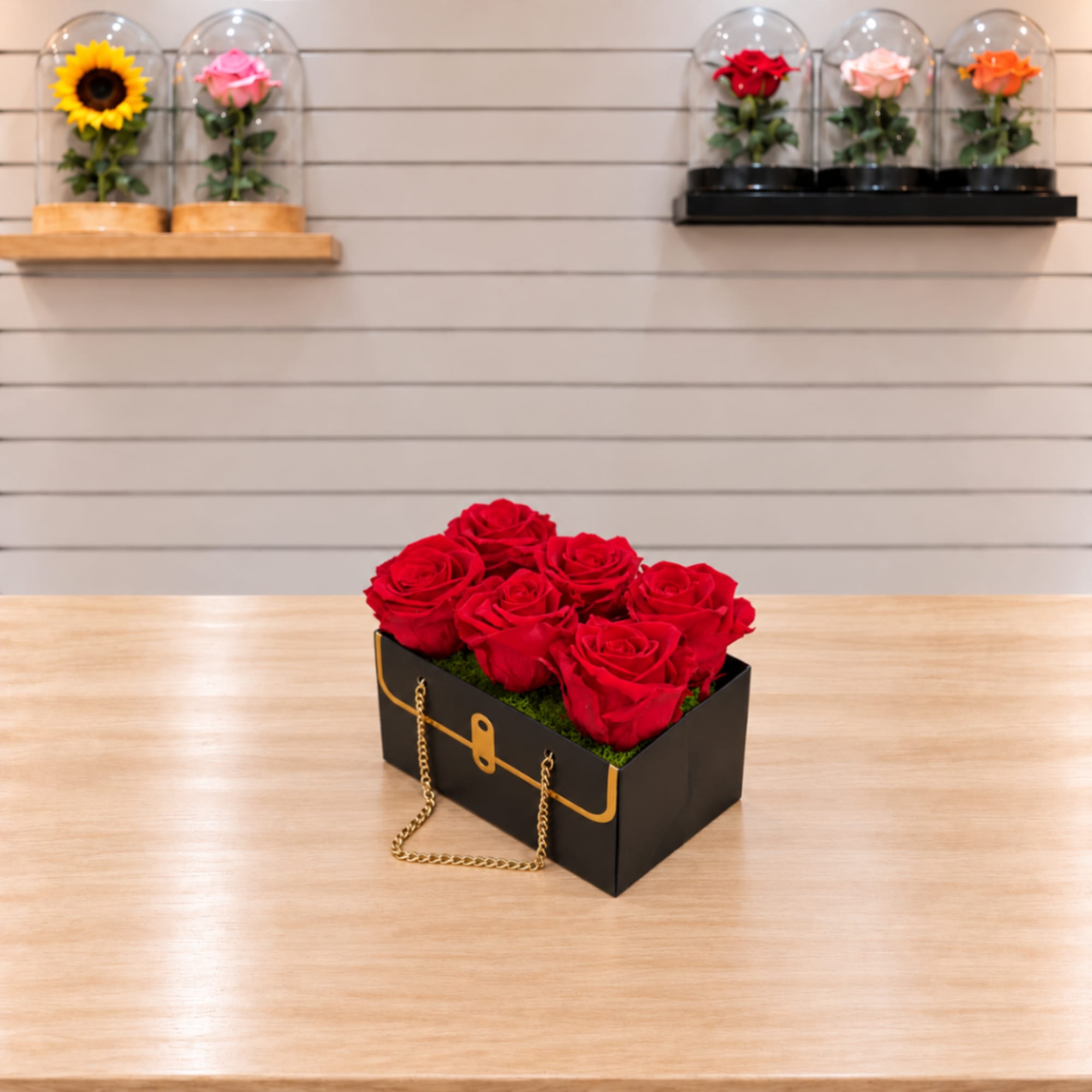 Red roses arranged in a black gift box with a gold chain handle
