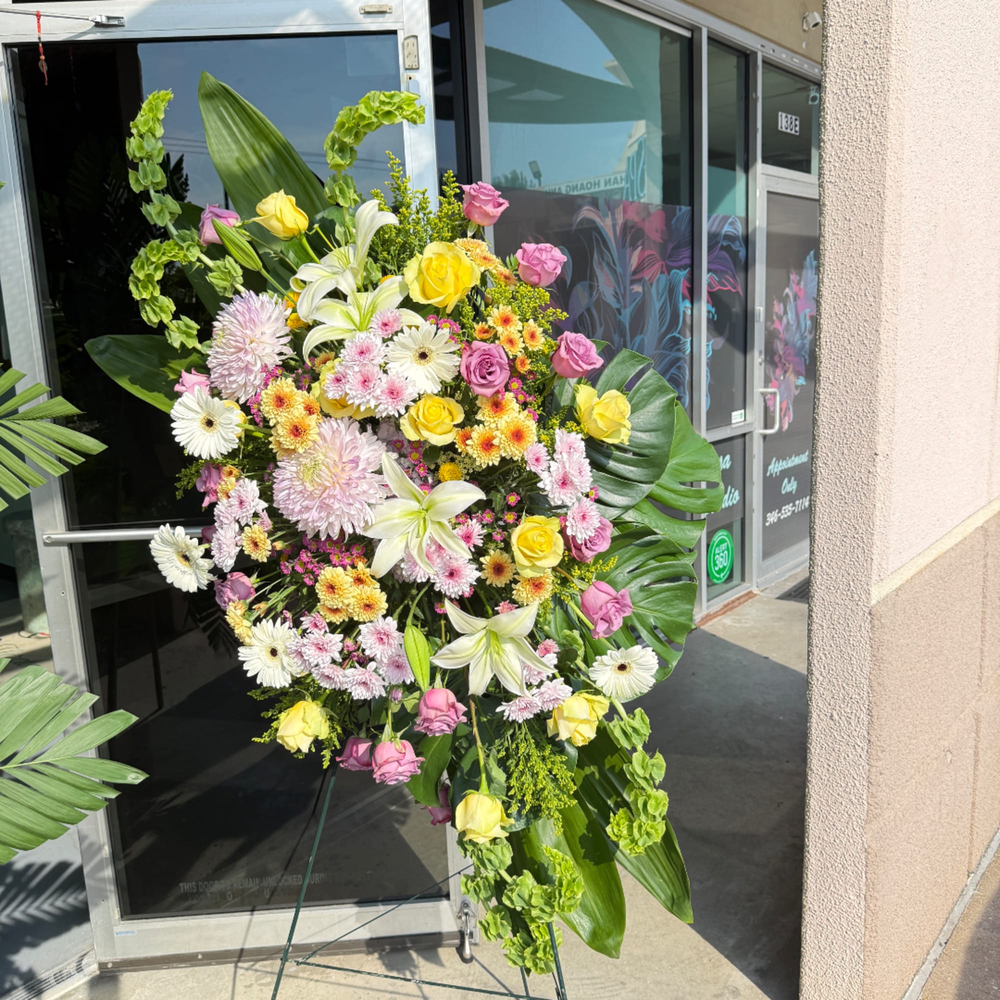 Large standing floral spray with roses, lilies, and daisies in pink, yellow, and white