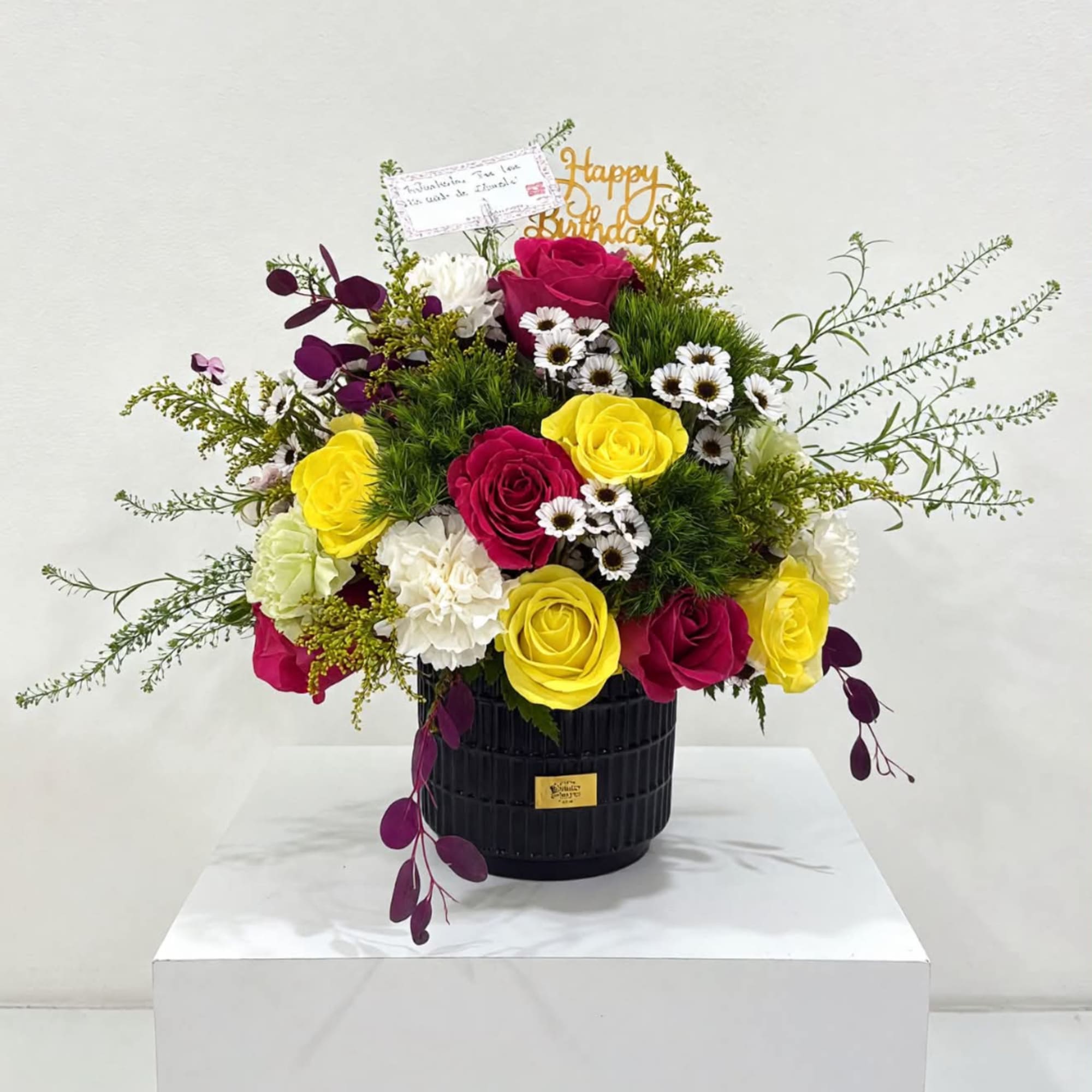 Mixed bouquet of roses and daisies in a black vase with a birthday topper