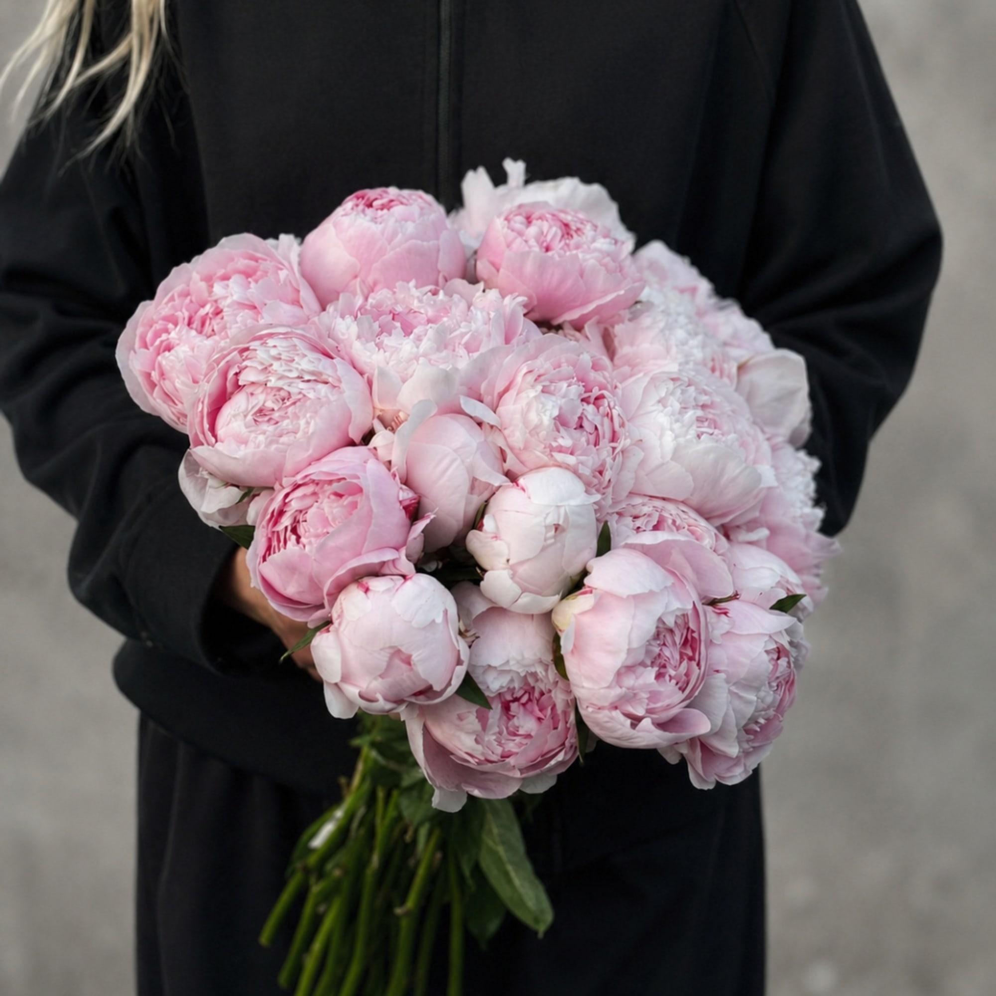 Person holding a bouquet of pale pink peonies