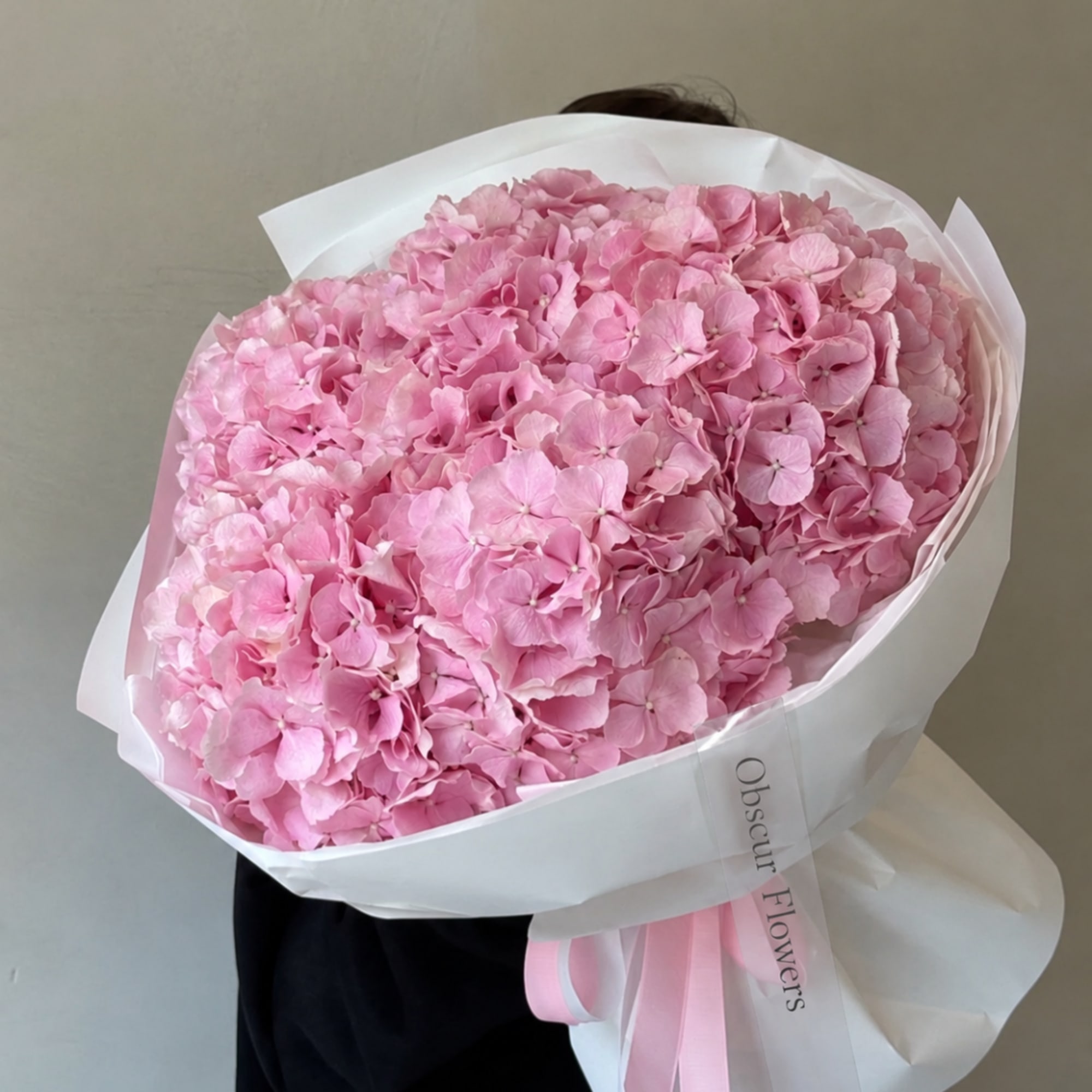 Large bouquet of pink hydrangeas wrapped in white paper with a pink ribbon