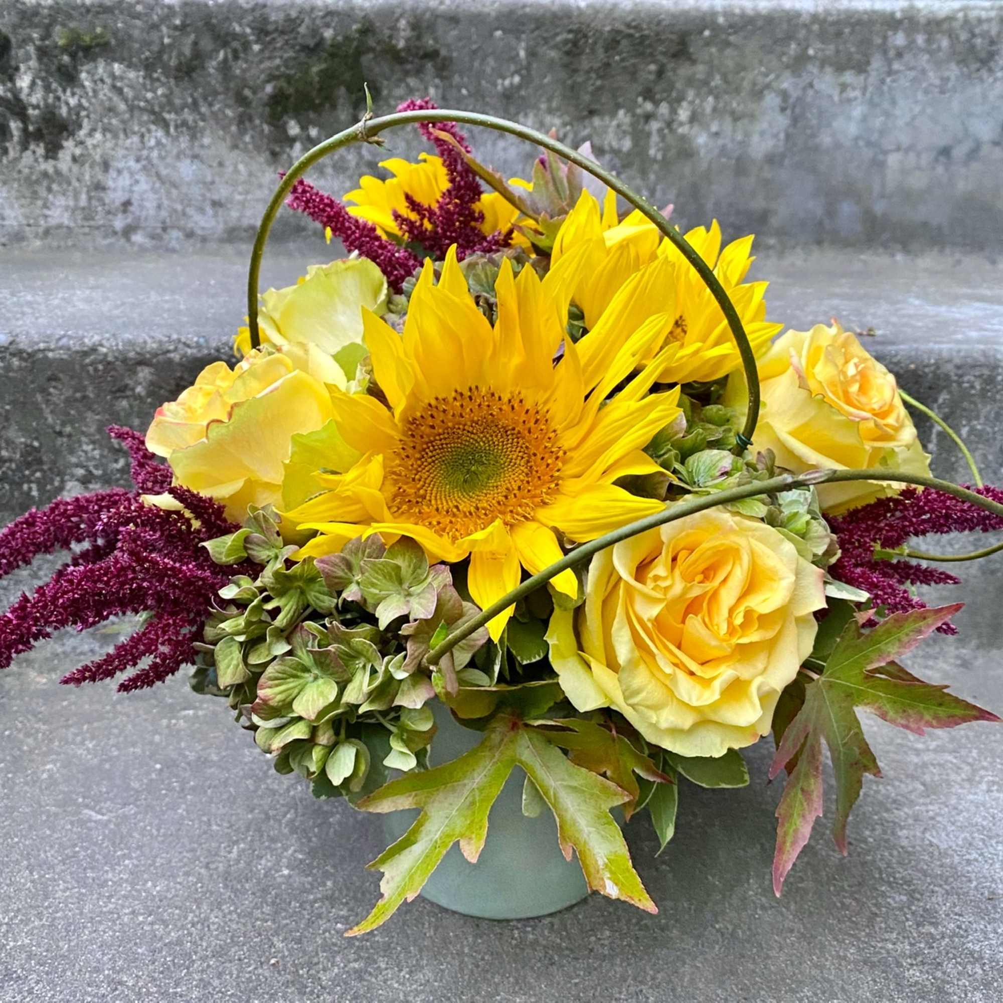 Yellow sunflower and roses in a small container with burgundy accents