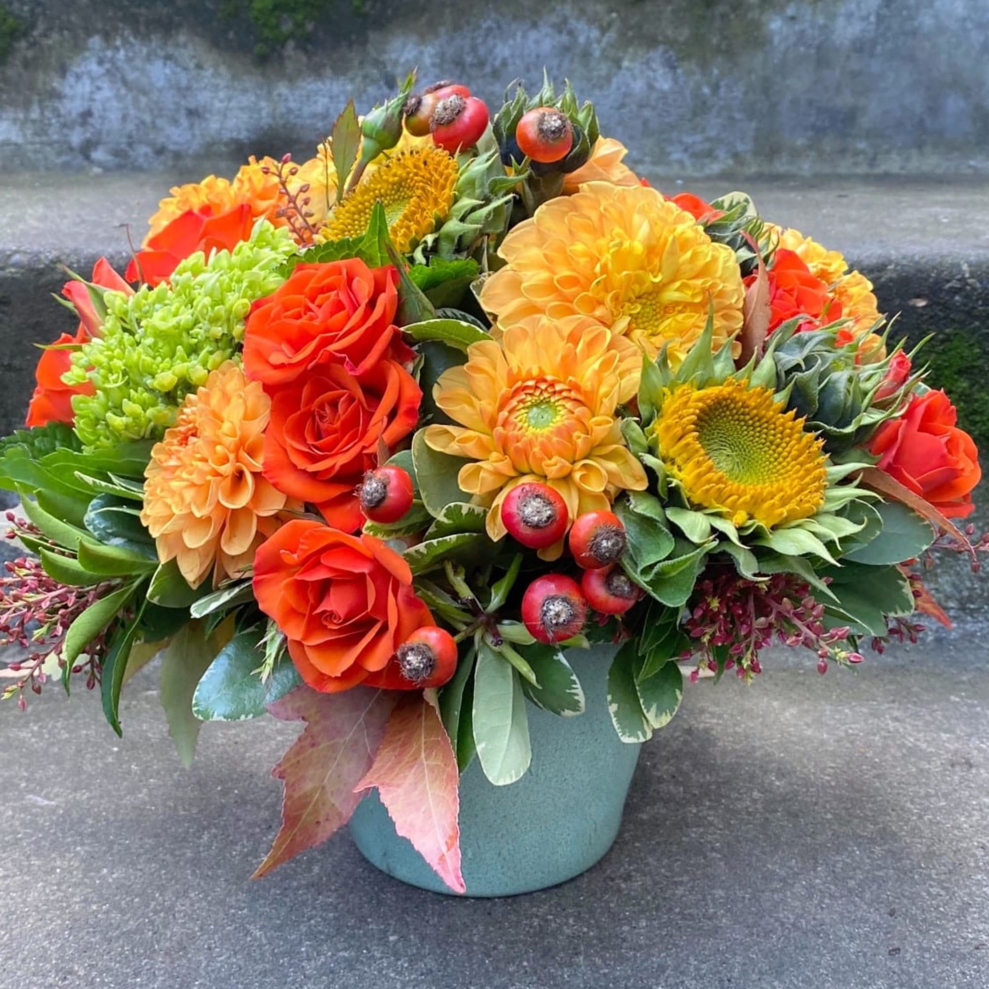 Orange and yellow flower arrangement in a teal container