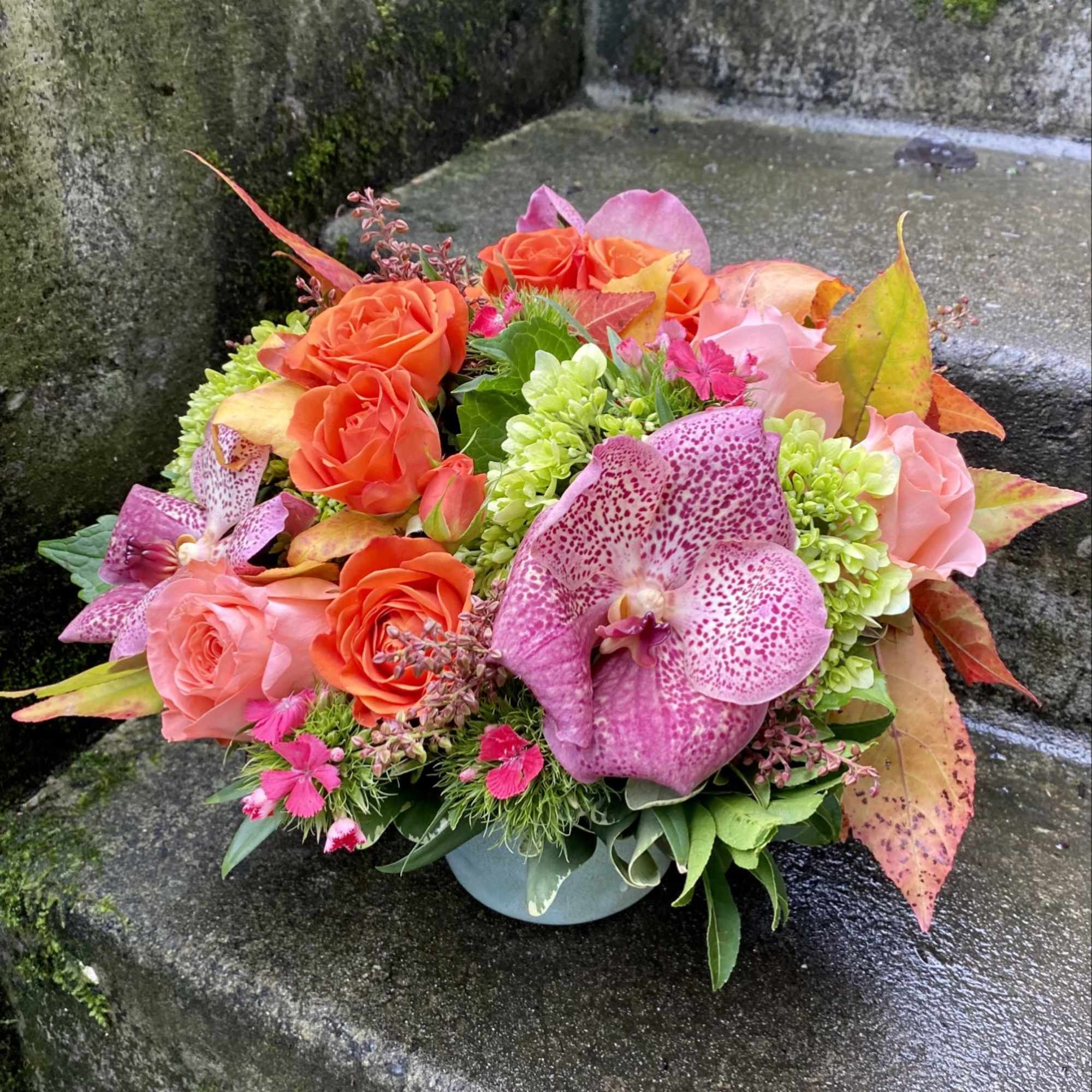 Bouquet of orange and pink roses with a spotted orchid in a low vase