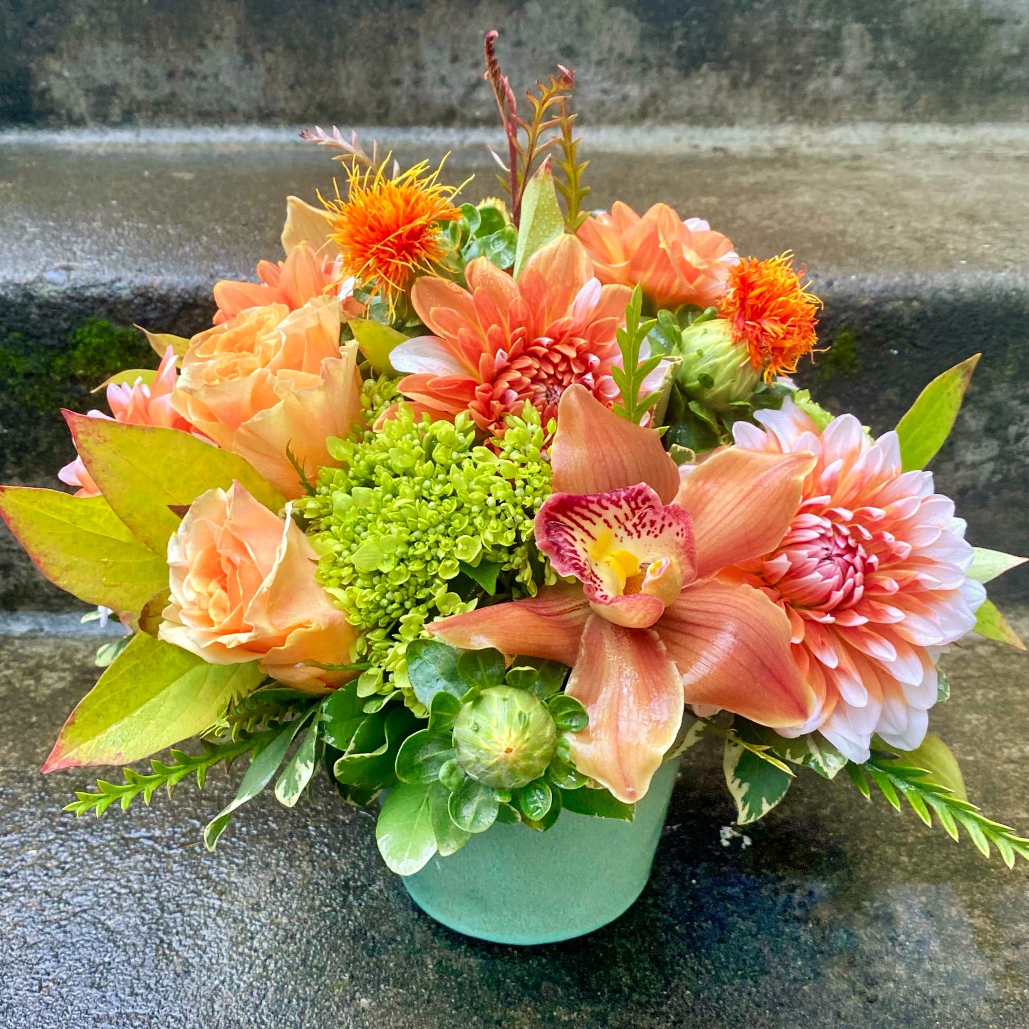 Peach and orange floral arrangement in a mint green vase