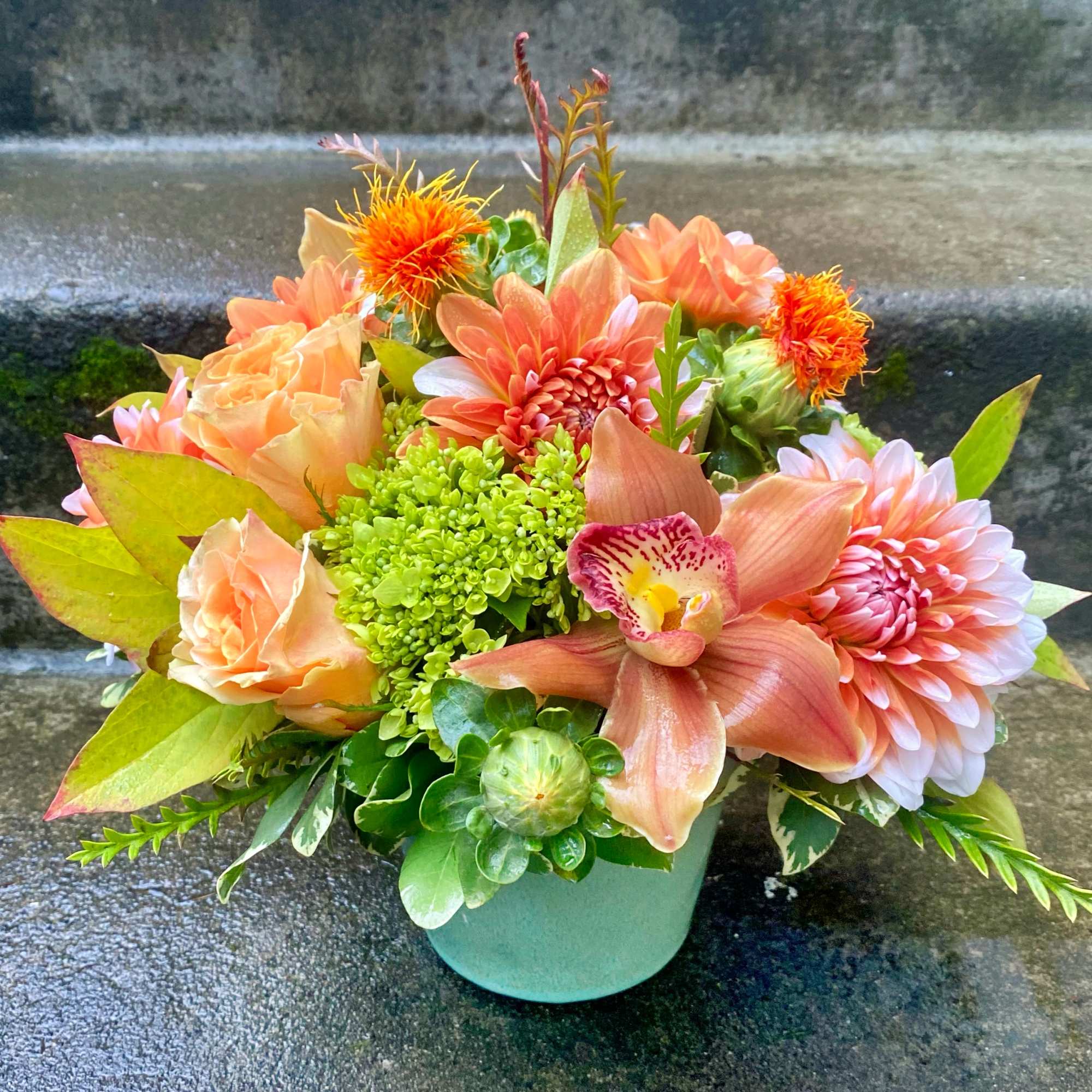 Peach and orange floral arrangement in a mint vase