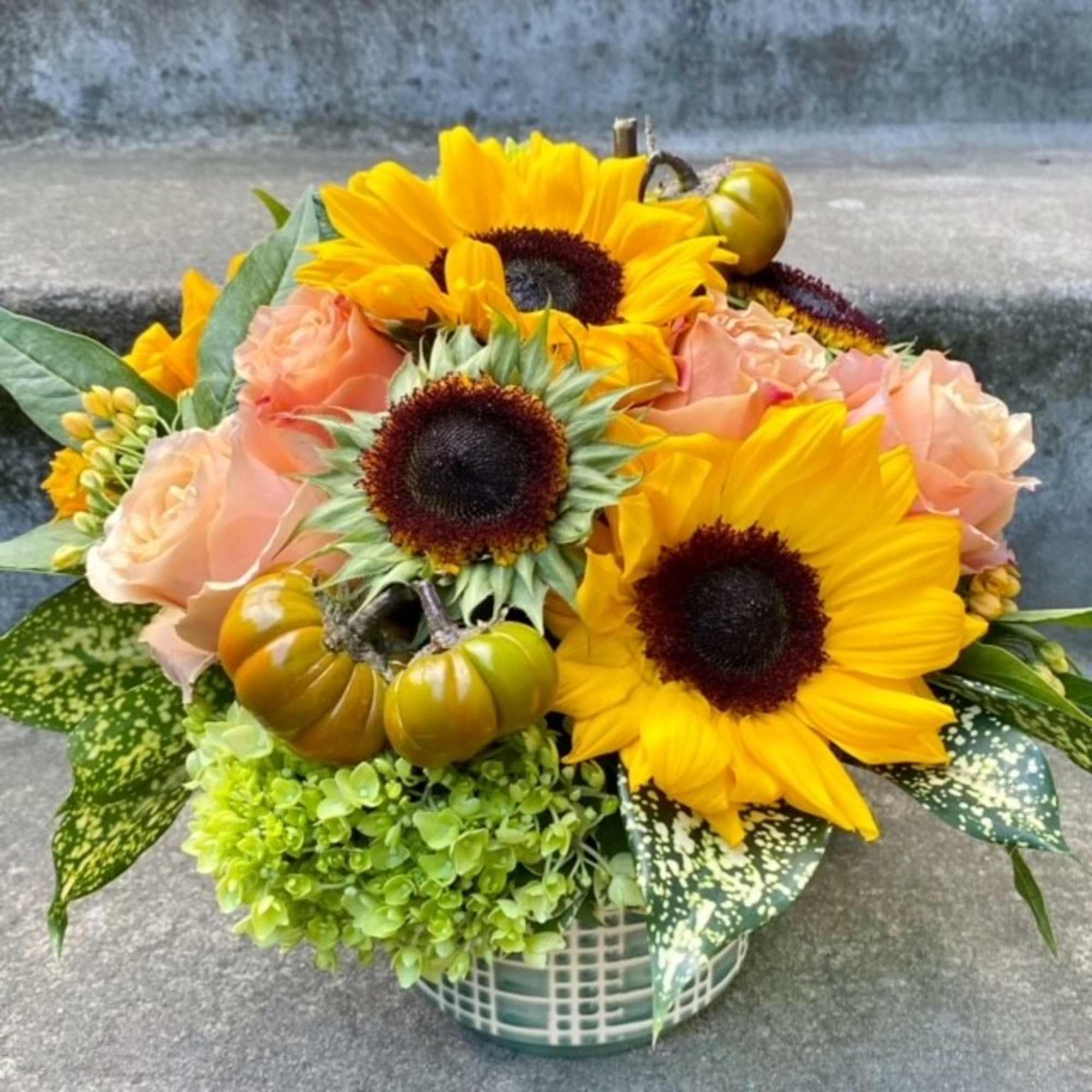 Sunflower and peach rose arrangement in a woven basket with small pumpkins