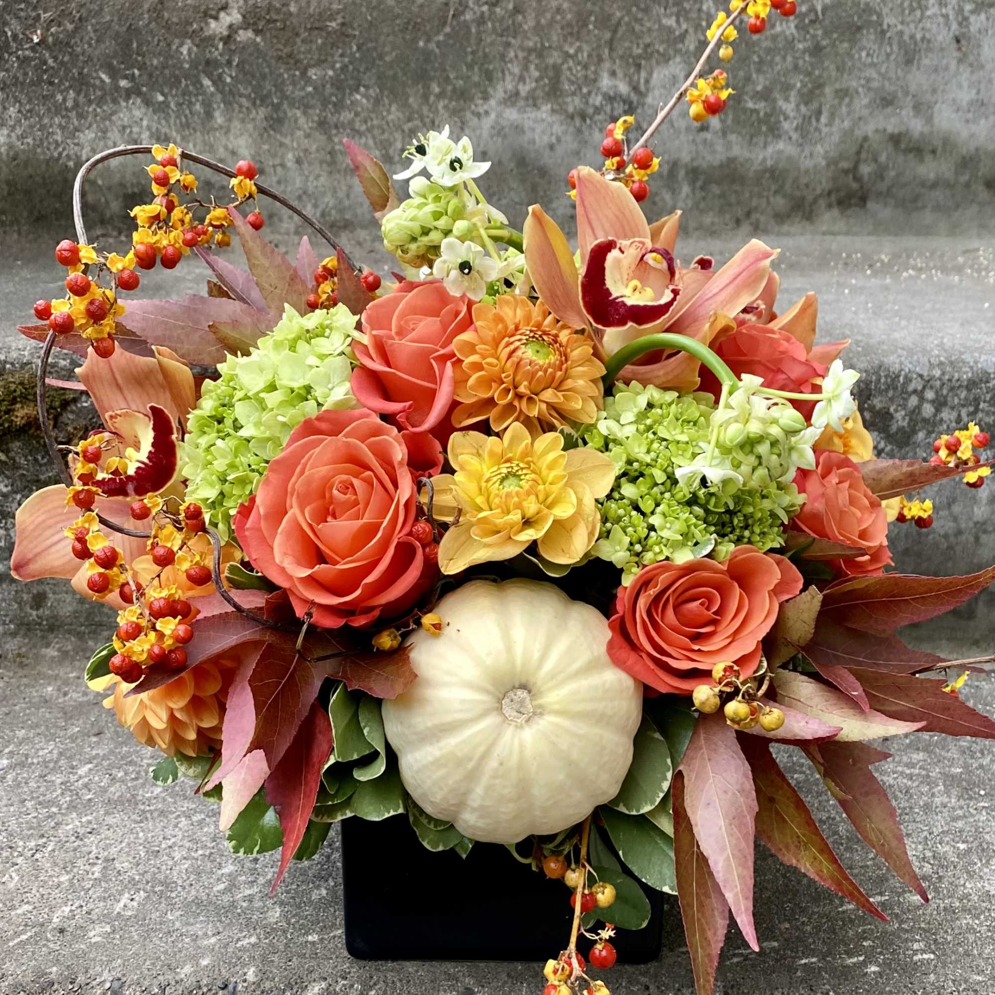 Autumn floral arrangement with roses, mums, hydrangea, and a white pumpkin in a black vase