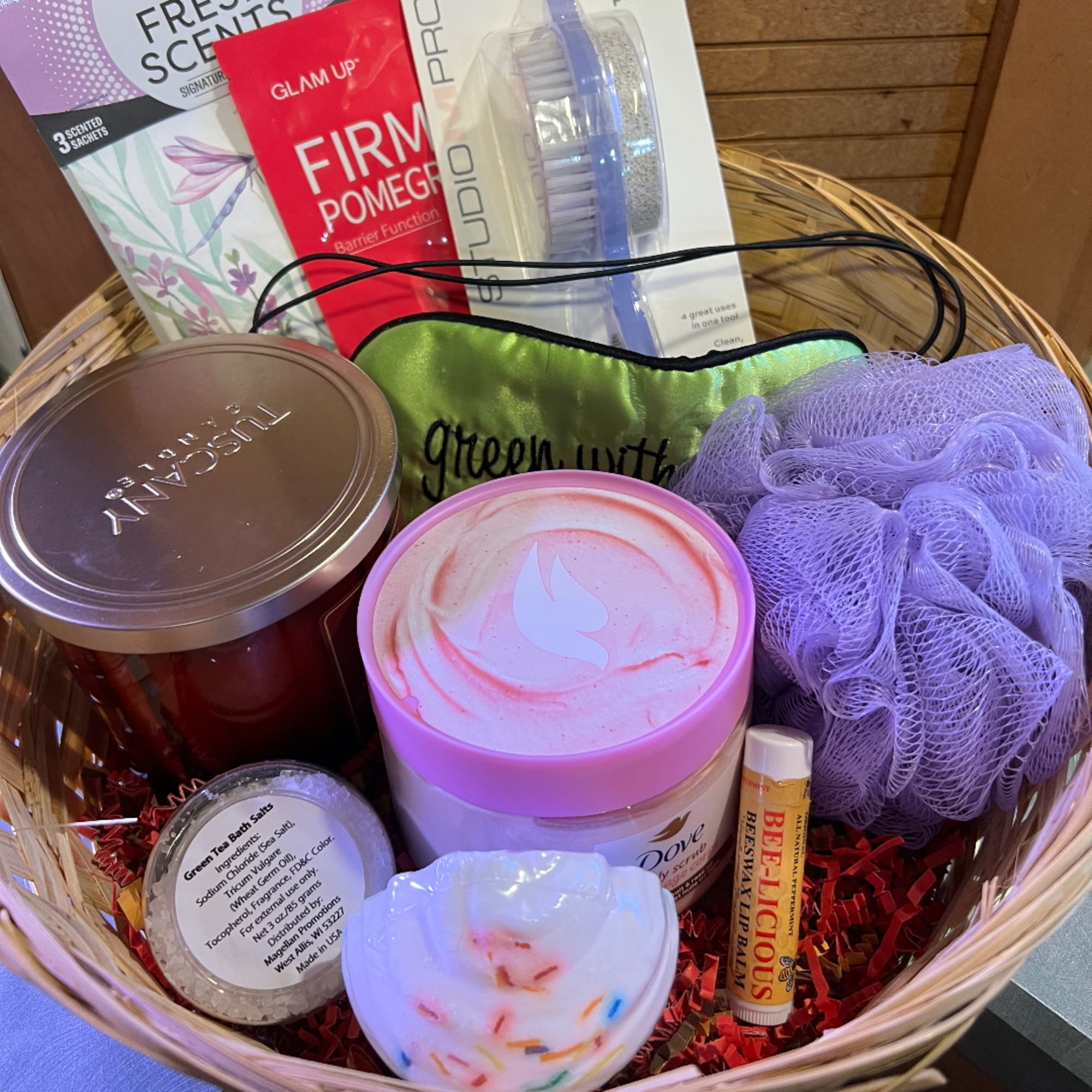 Basket of bath and body gifts with candles, scrub, lip balm, and a loofah