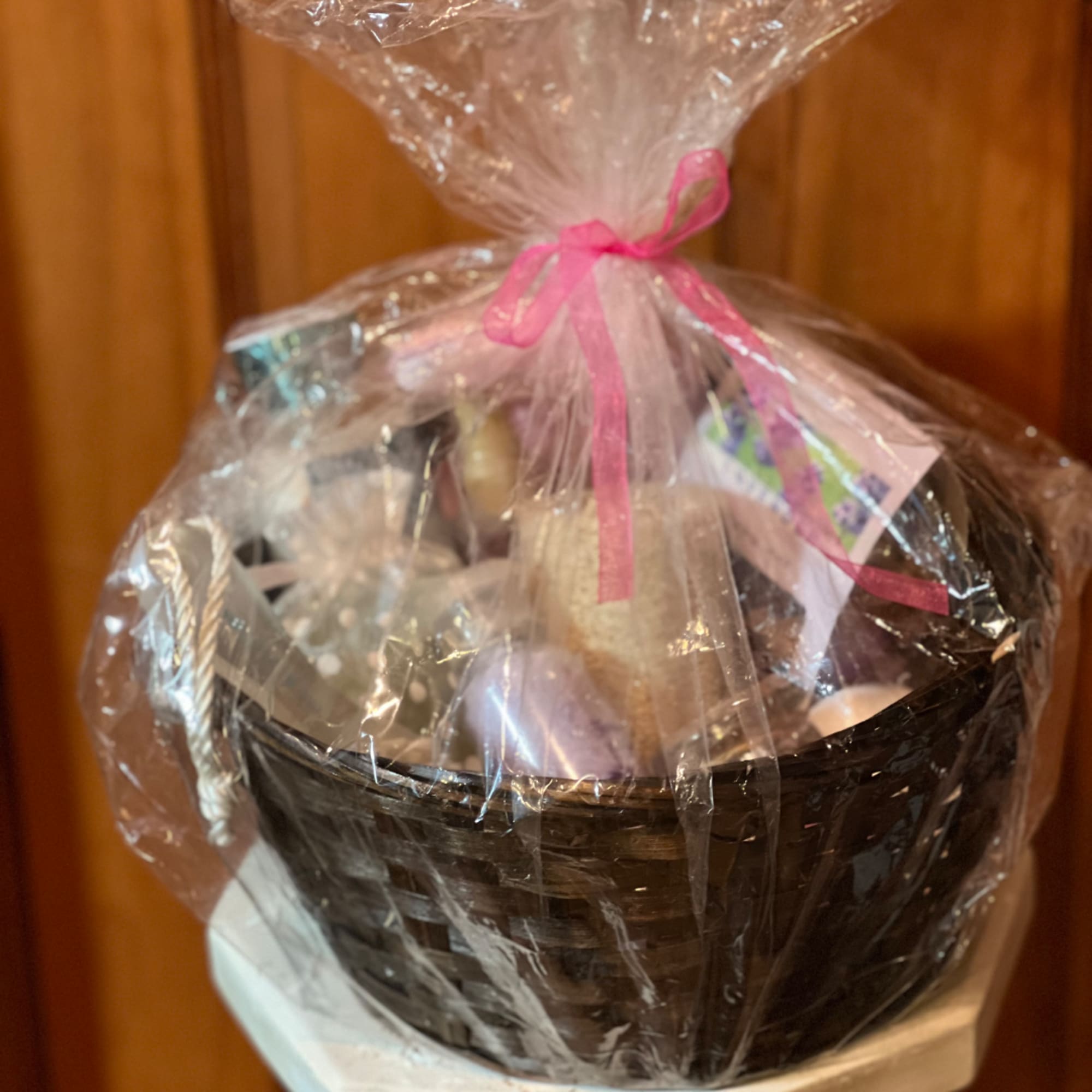Gift basket wrapped in clear cellophane with a pink ribbon