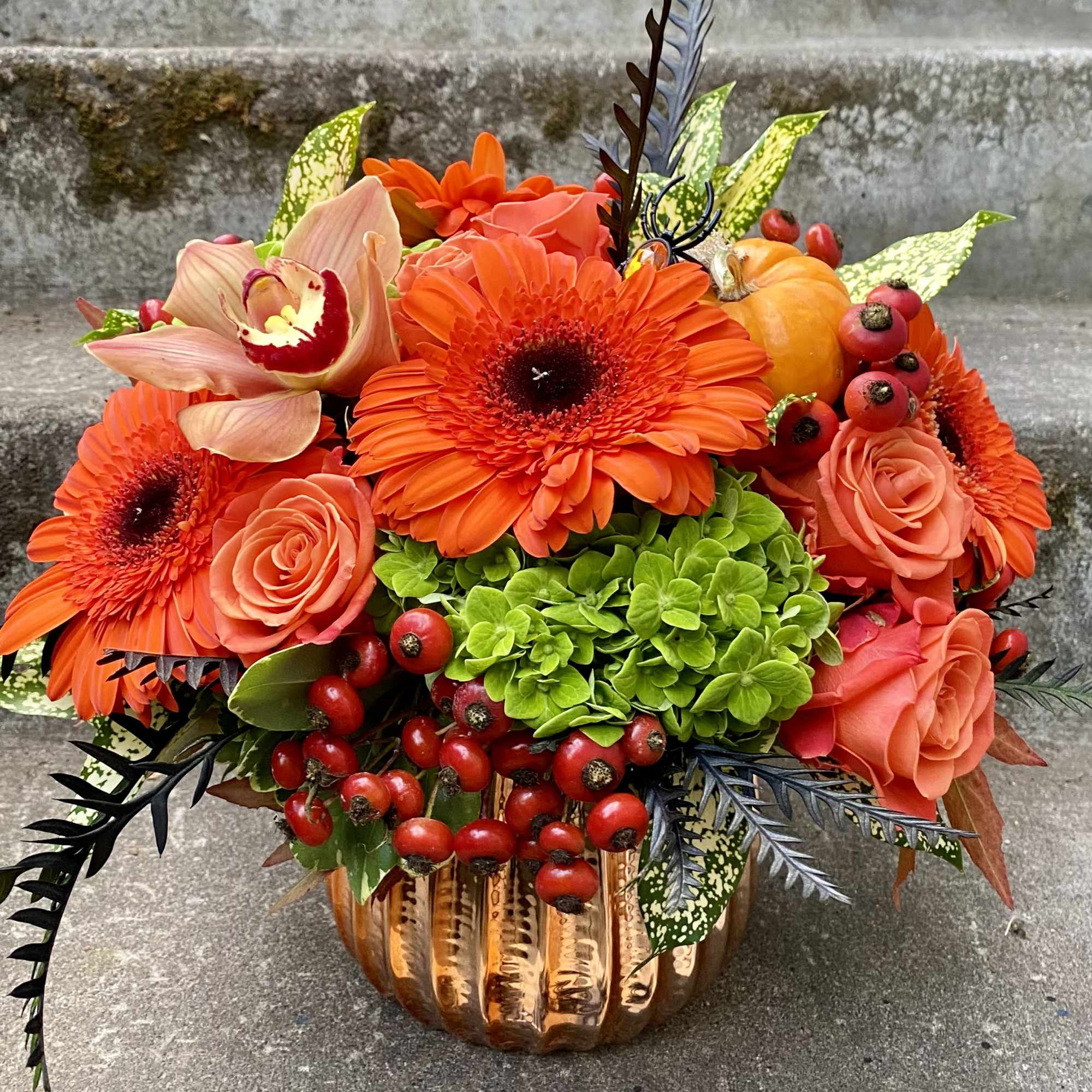 Orange floral arrangement in a copper pumpkin vase with roses and gerbera daisies