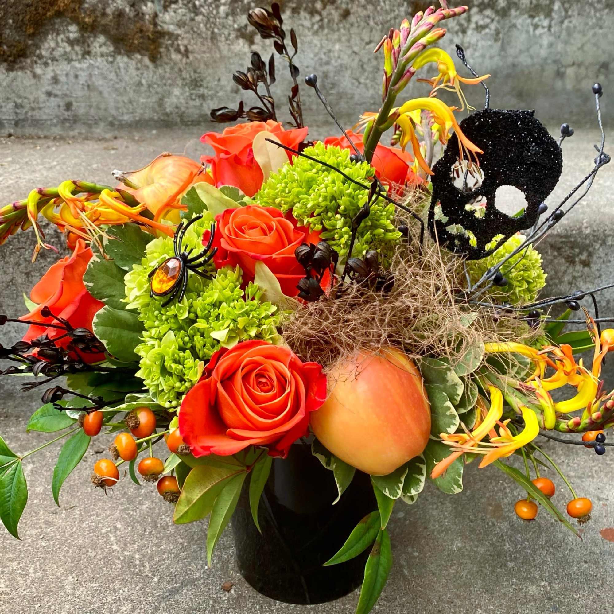 Orange roses and Halloween accents in a black vase