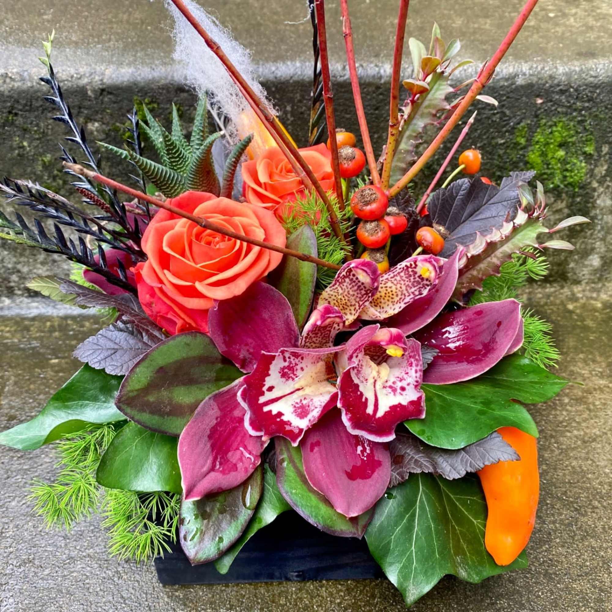 Orange roses and purple orchids in a low black container