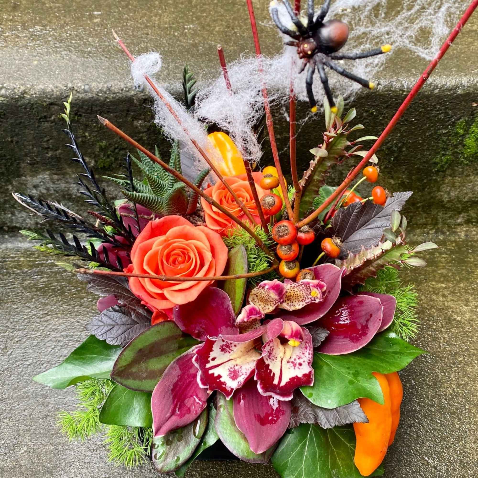 Orange roses and burgundy orchids in a low arrangement with Halloween accents