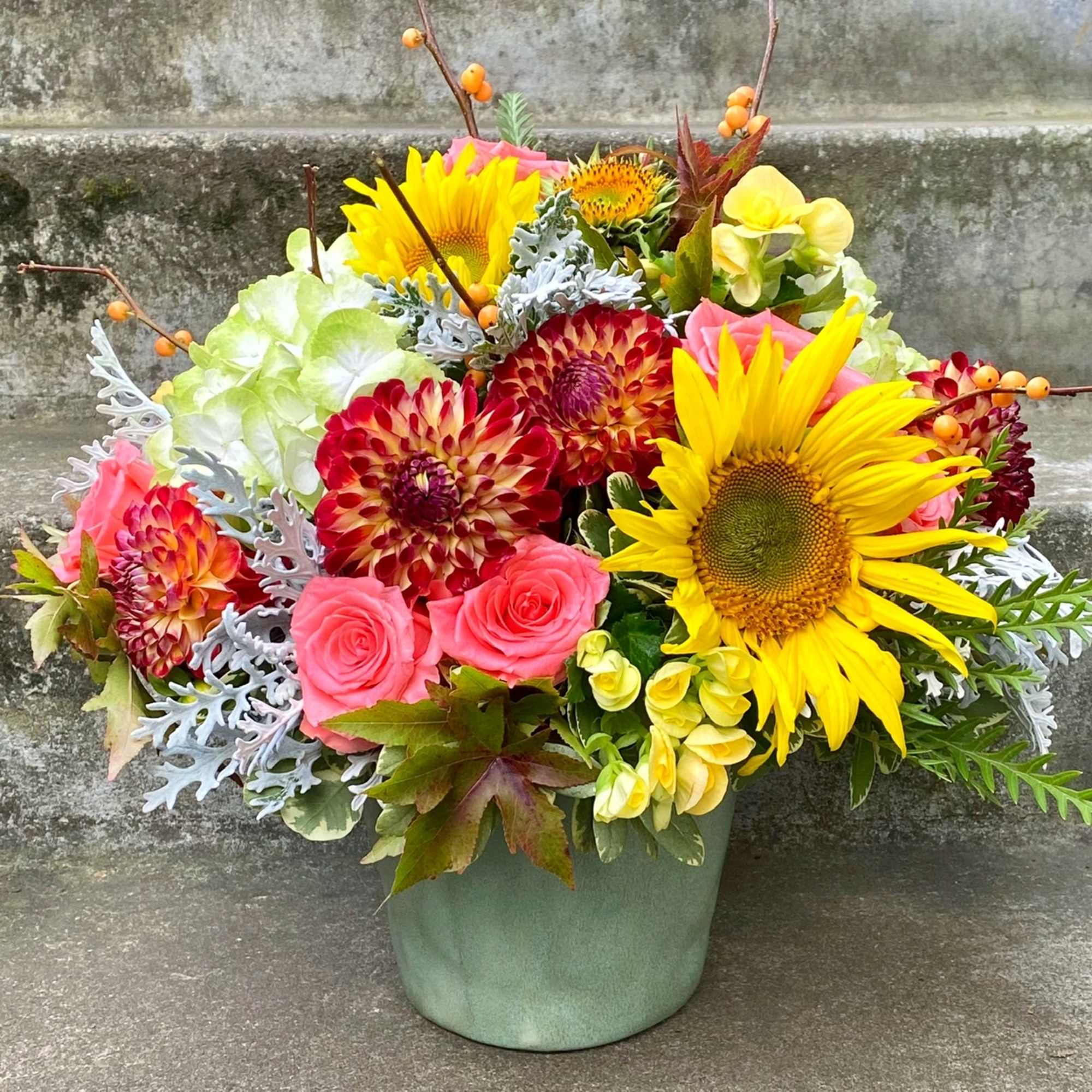 Bright mixed bouquet in a green container with sunflowers and pink roses