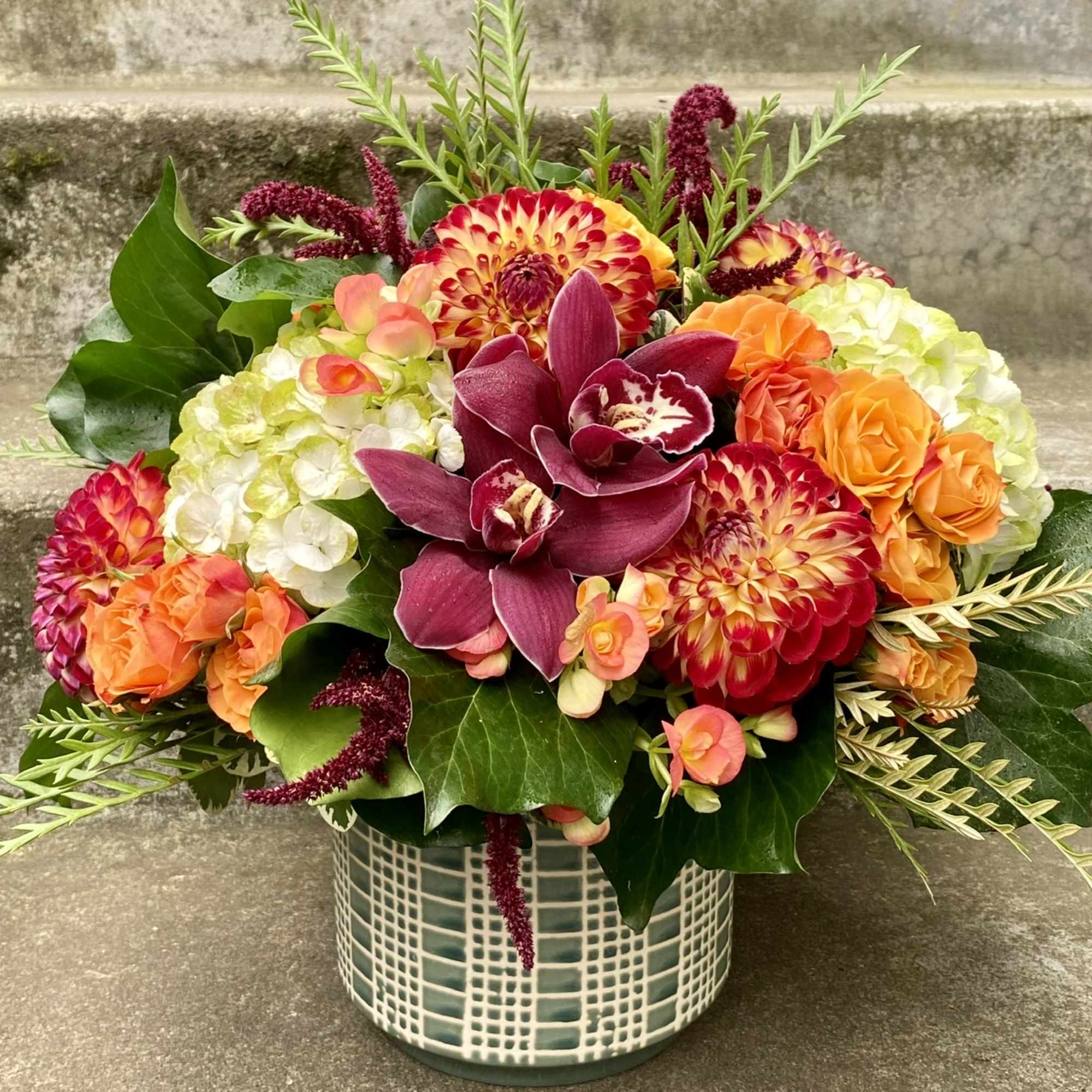 Mixed floral arrangement in a patterned ceramic vase with orange, burgundy, and white blooms.