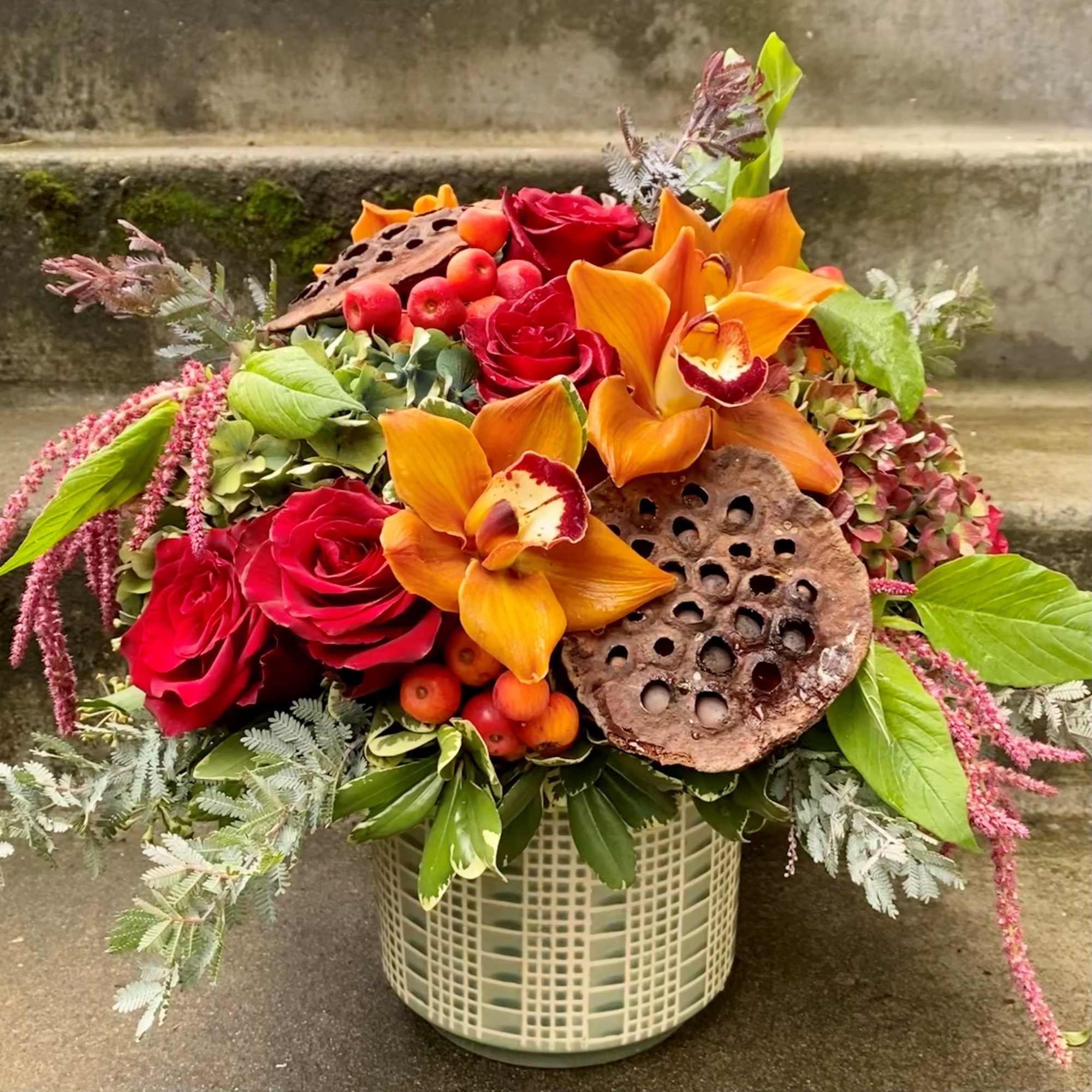 Bouquet of red roses and orange orchids in a woven vase
