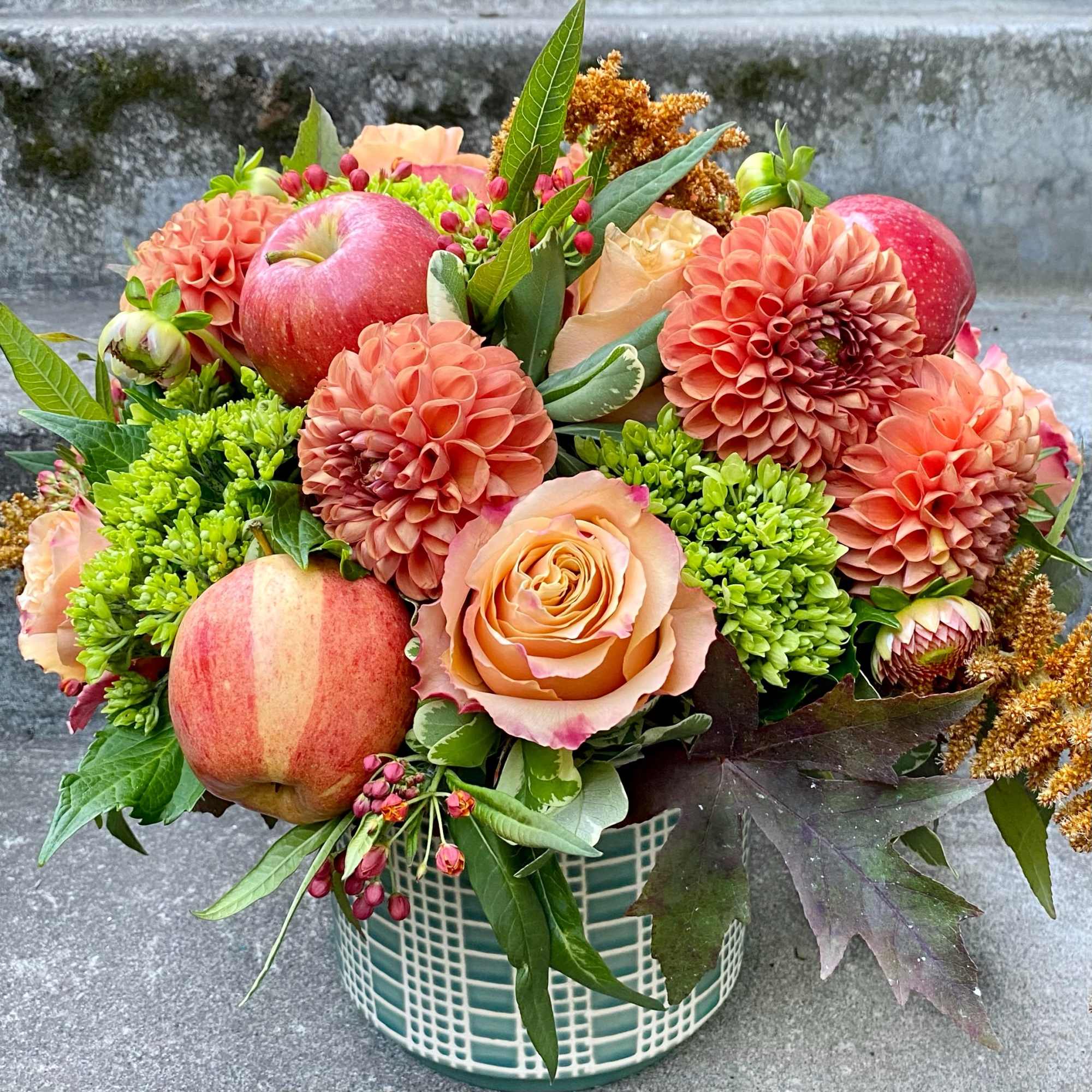 Peach and coral floral arrangement with apples in a mosaic vase