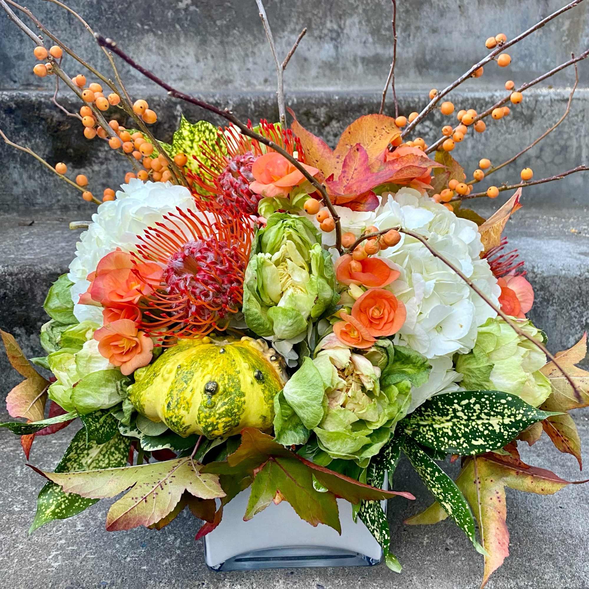 Autumn floral arrangement with hydrangeas, orange blooms, berries, and a gourd in a vase