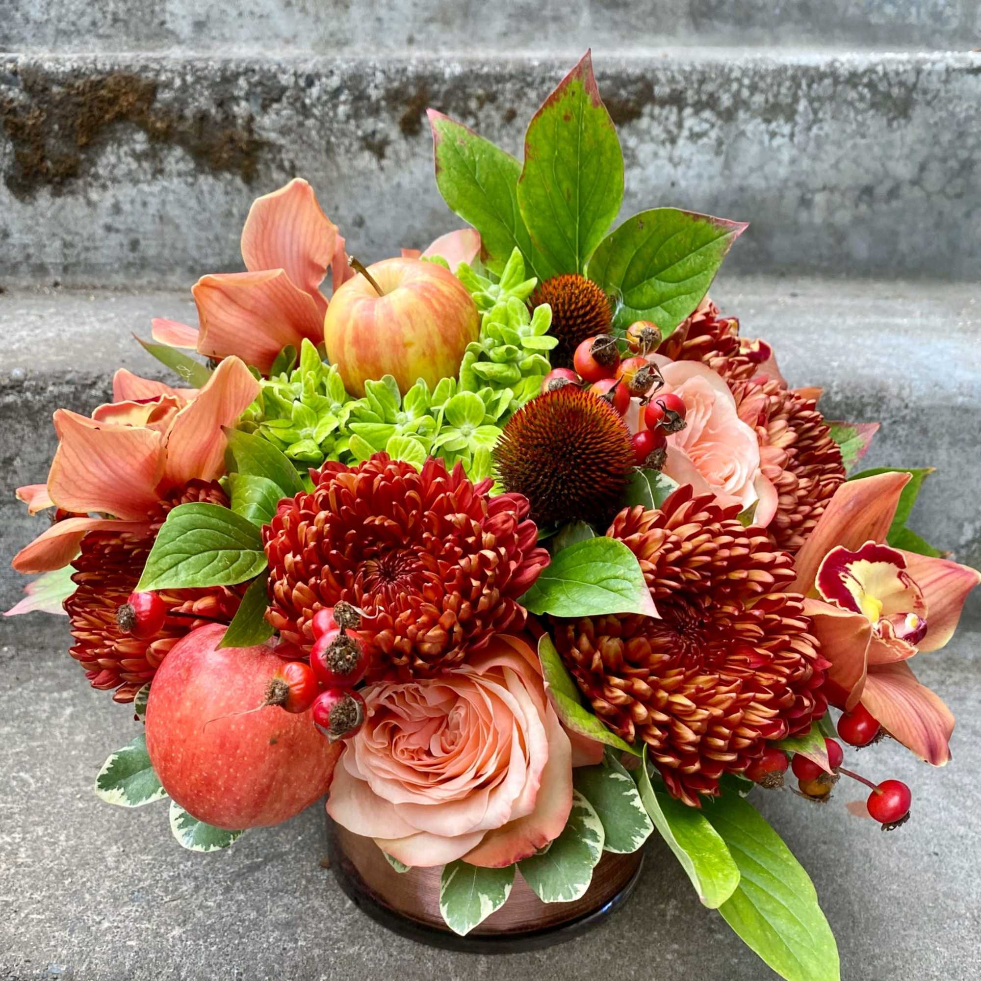 Autumn bouquet with peach roses, orange mums, apples, and berries in a low vase