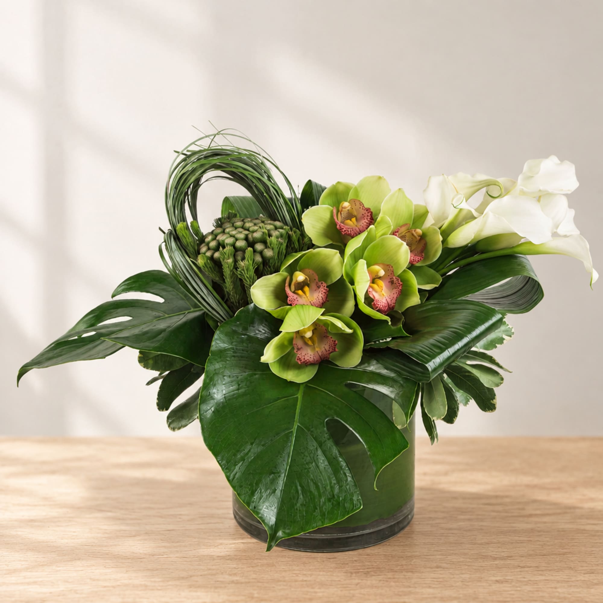 Green orchid arrangement in a glass vase with large tropical leaves