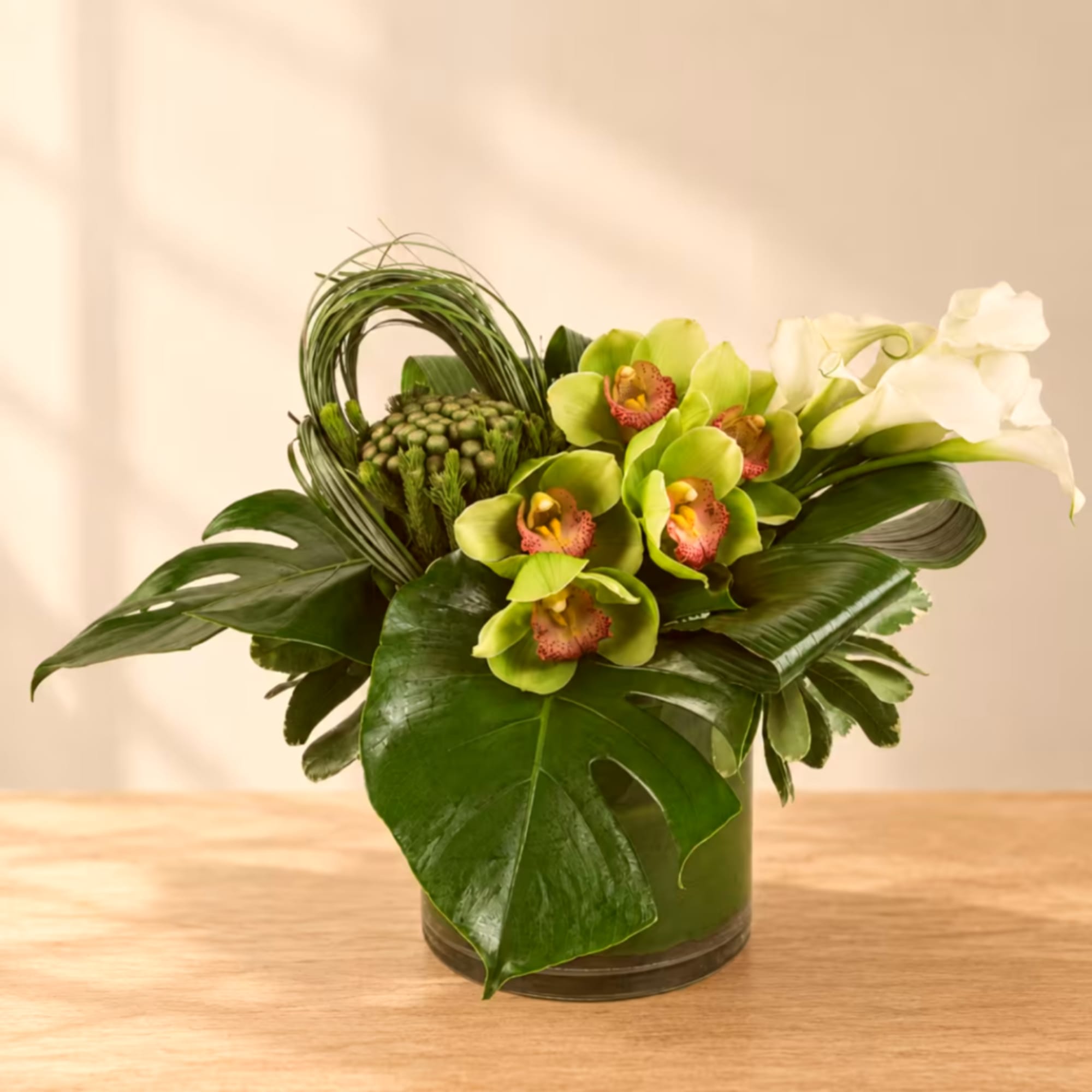 Green orchid arrangement in a glass vase with large tropical leaves, photo 4 of 4