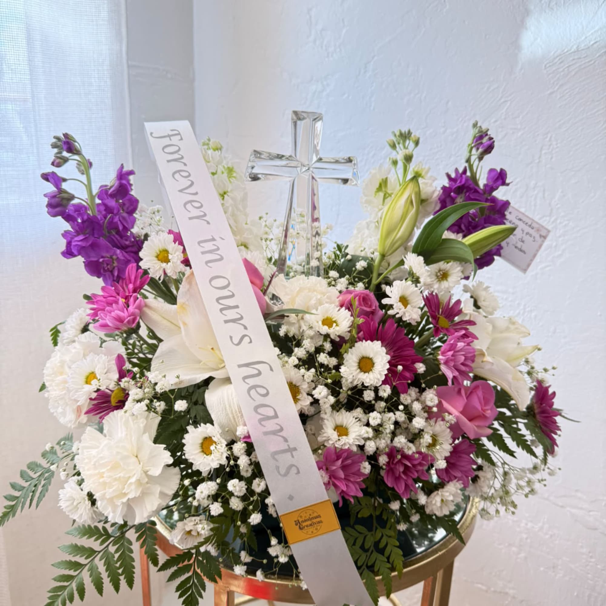 Mixed white and purple floral arrangement with a clear cross and memorial ribbon