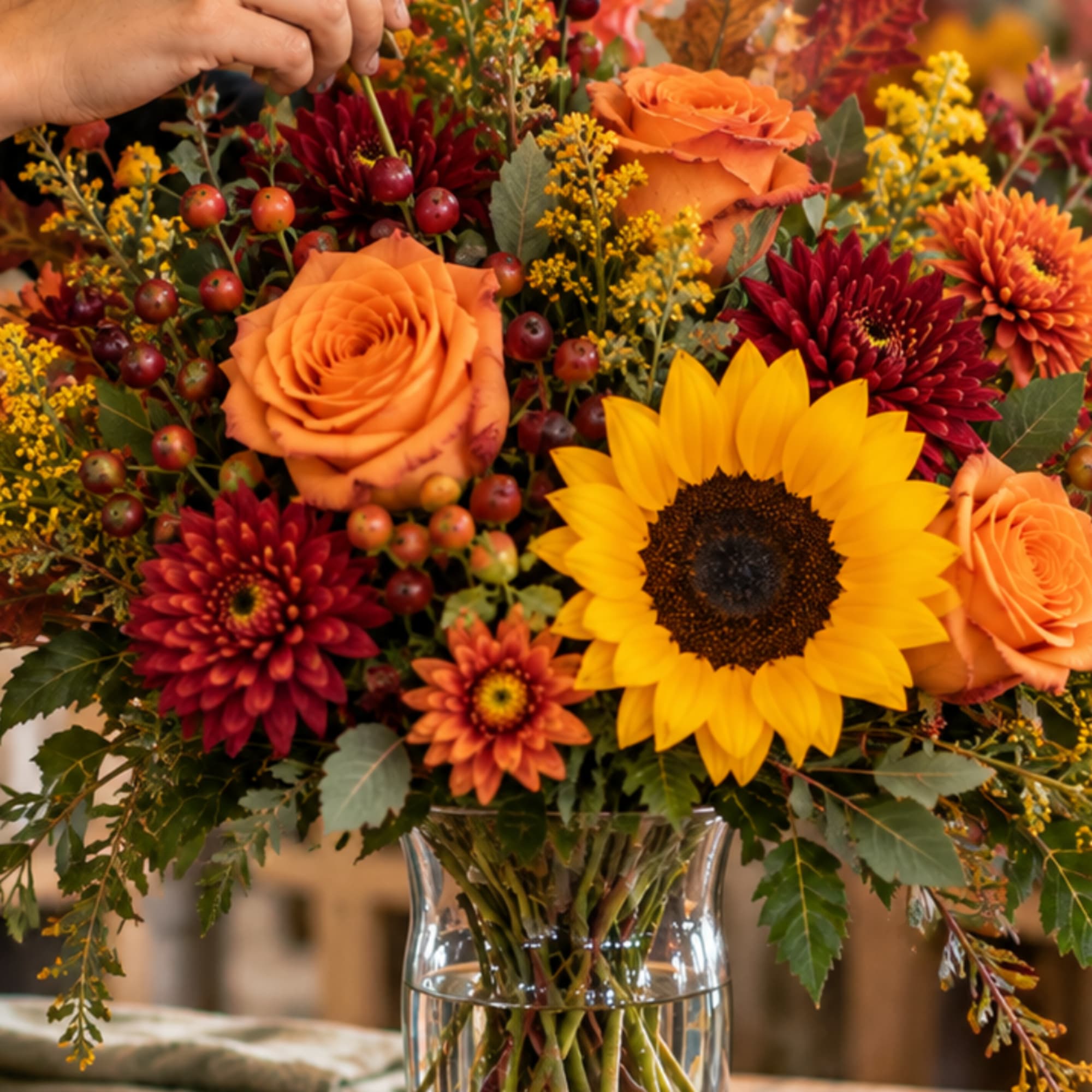 Bouquet of orange roses, sunflowers, and burgundy mums in a glass vase