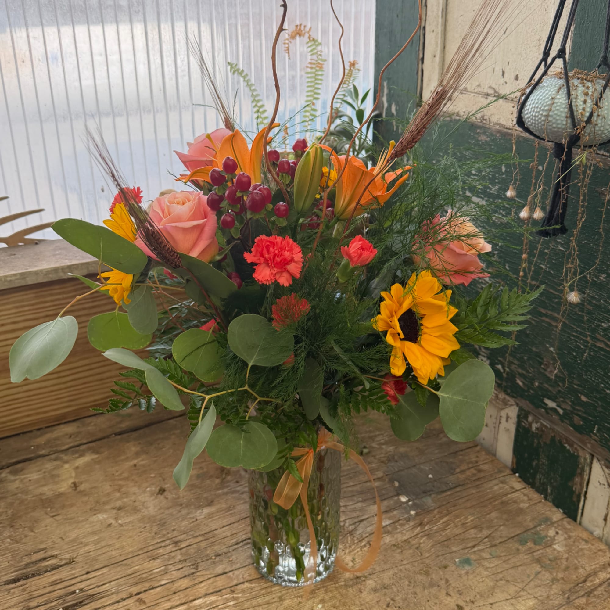 Mixed bouquet with roses, lilies, sunflowers, and carnations in a glass vase