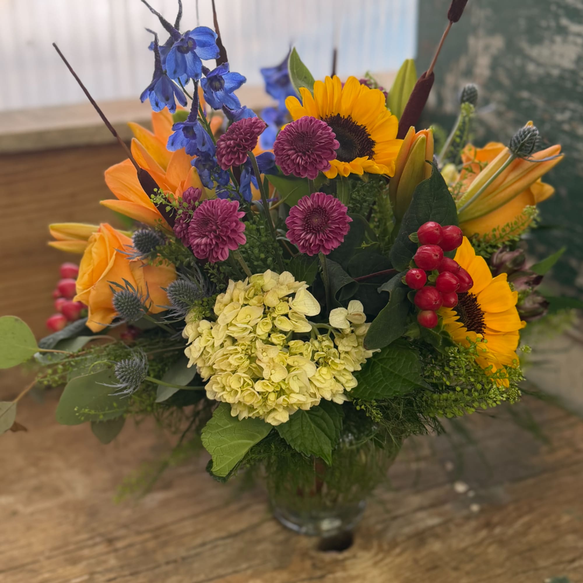 Mixed bouquet with sunflowers, blue delphinium, roses, and hydrangea in a glass vase