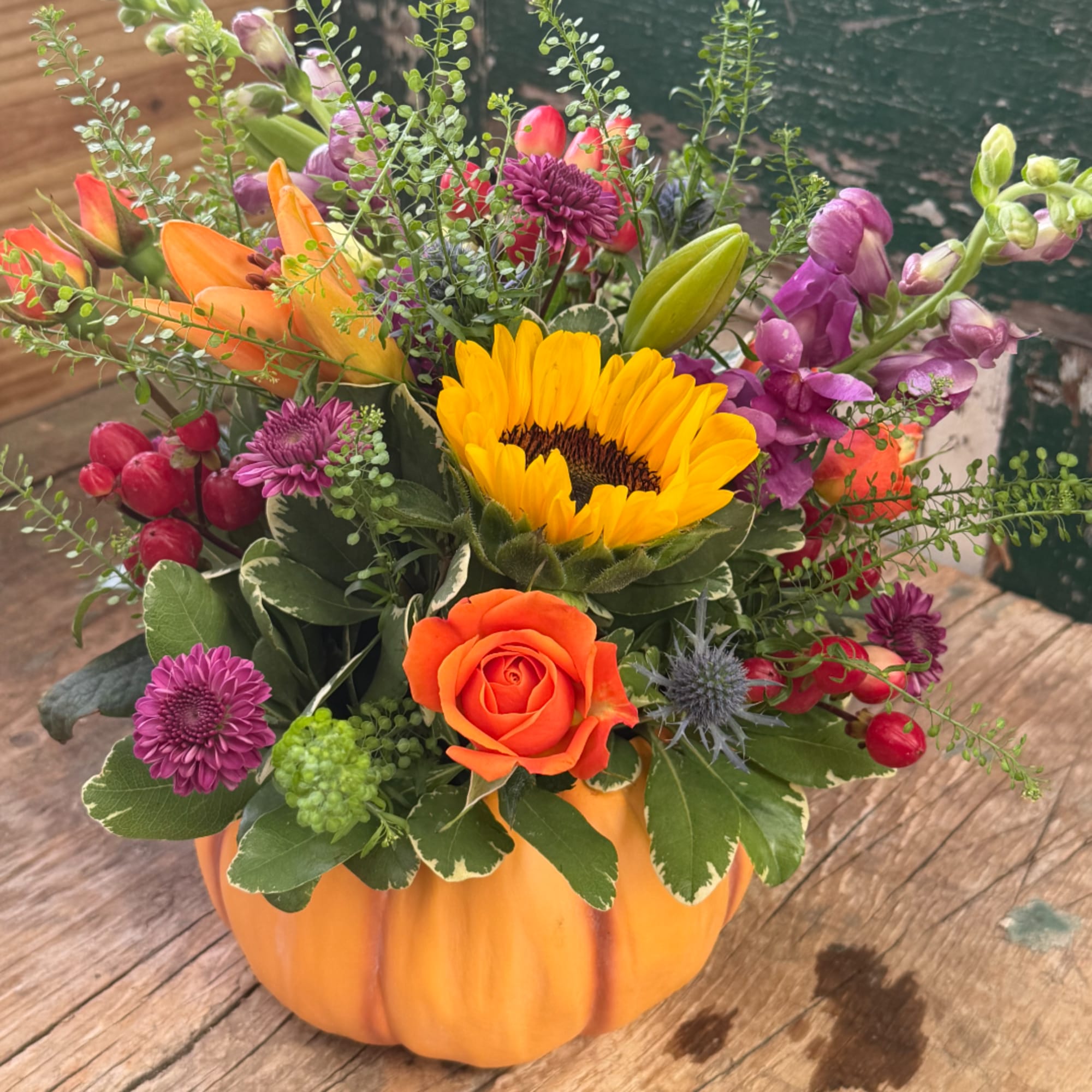 Mixed bouquet in a pumpkin-shaped container with a sunflower and orange rose