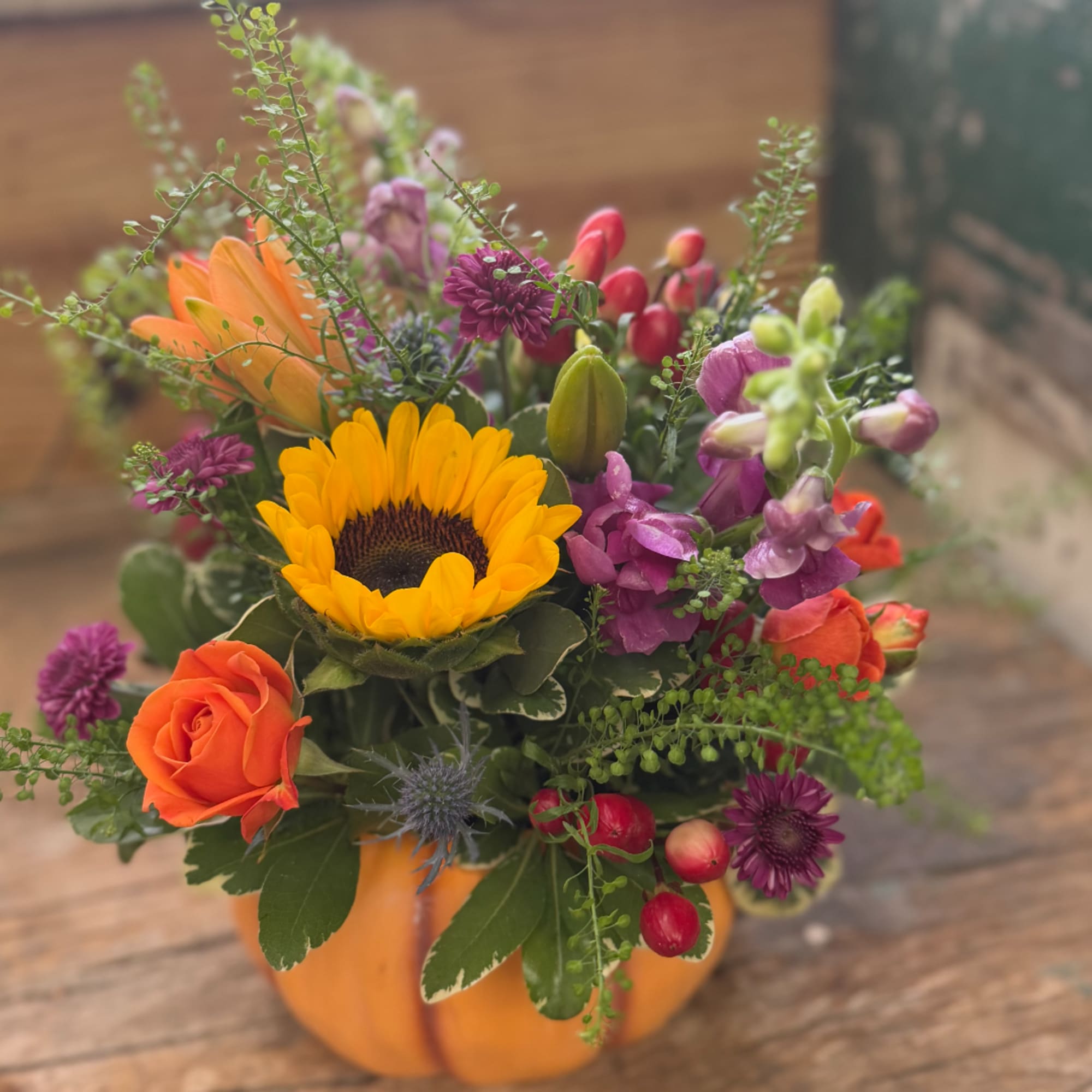 Mixed bouquet in a small pumpkin-shaped container with a sunflower and orange rose