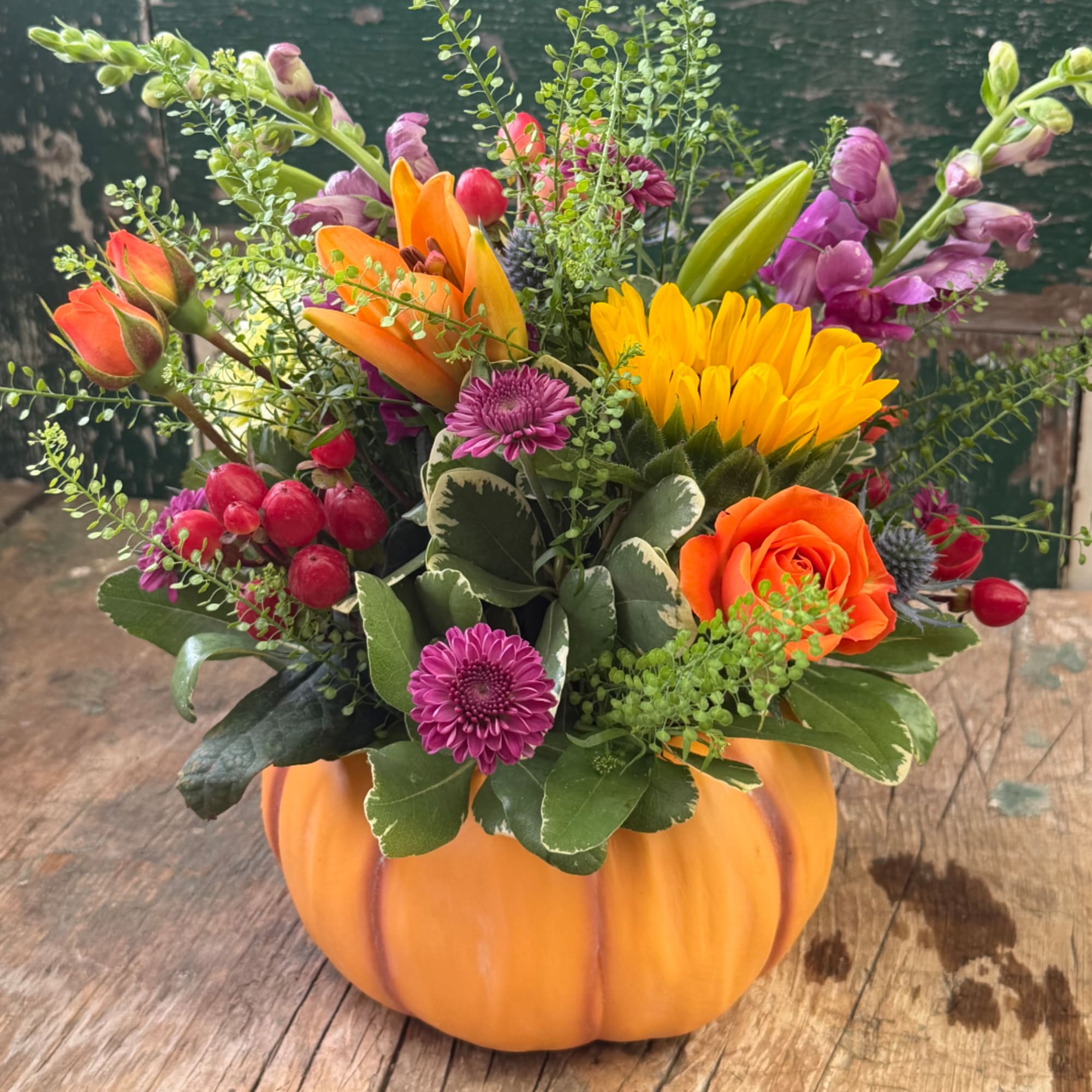 Mixed bouquet in a pumpkin-shaped container with orange, yellow, and purple flowers
