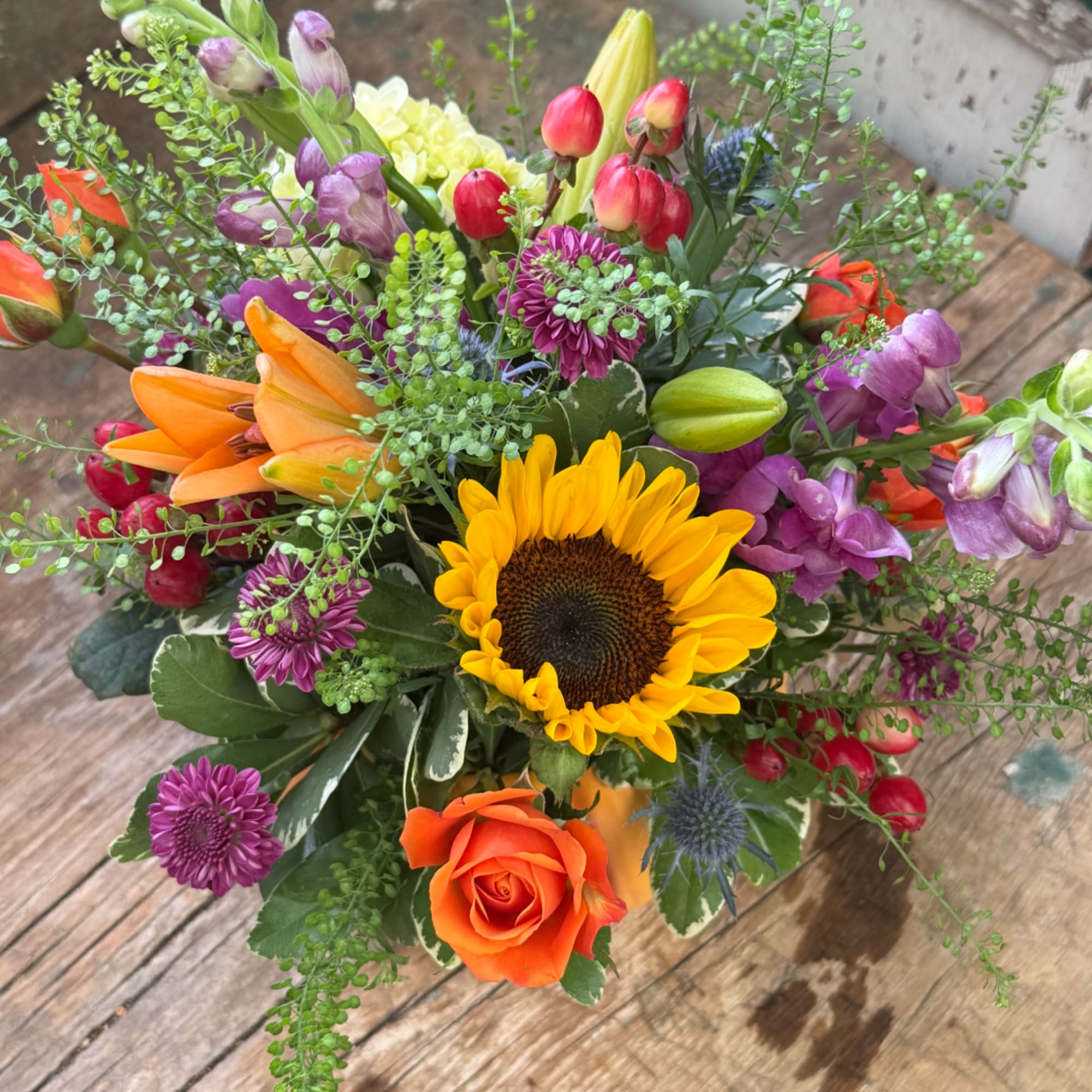 Mixed bouquet with a sunflower, orange rose, lilies, and purple blooms